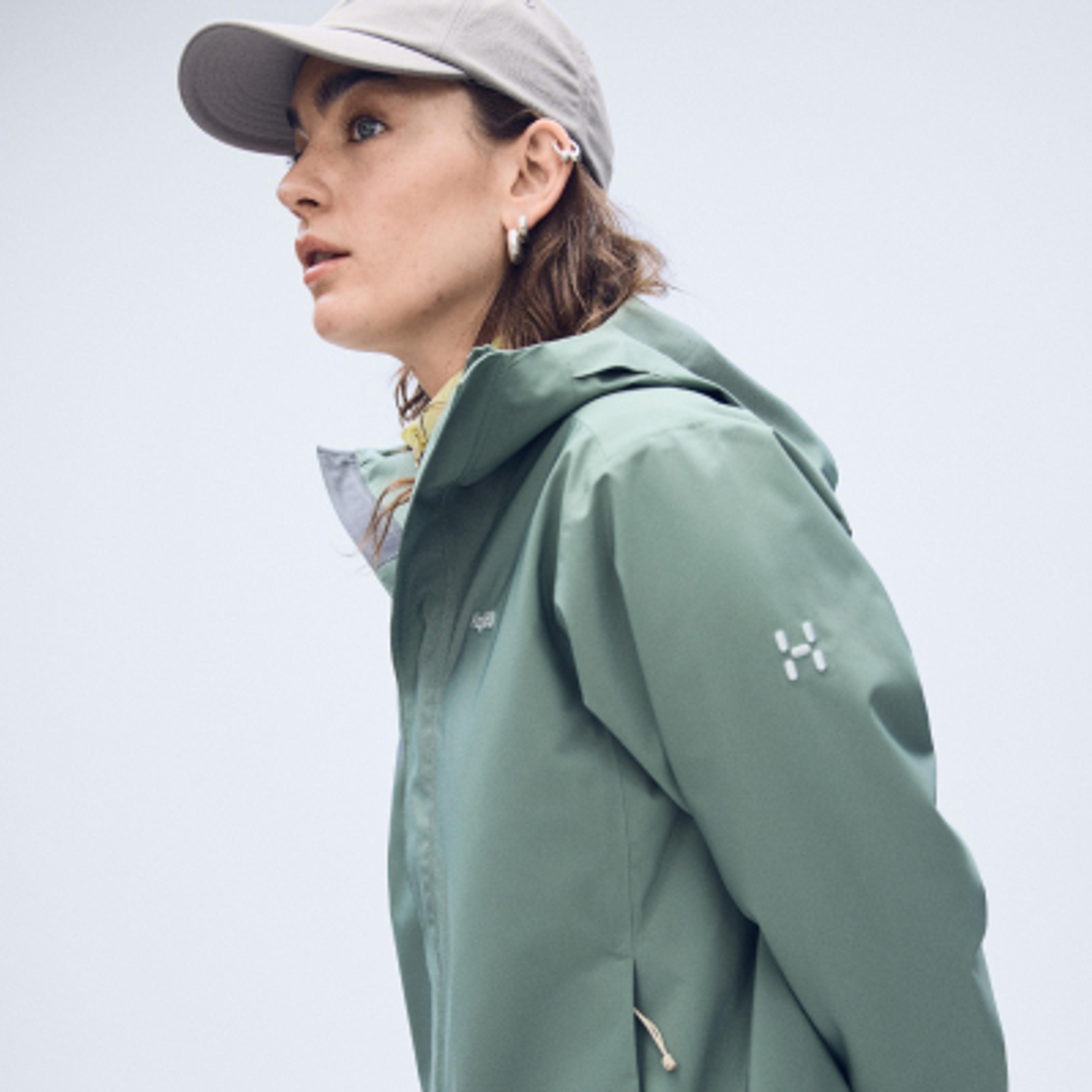 Woman wearing a grey cap and a sage green Haglöfs outdoor jacket, looking left.
