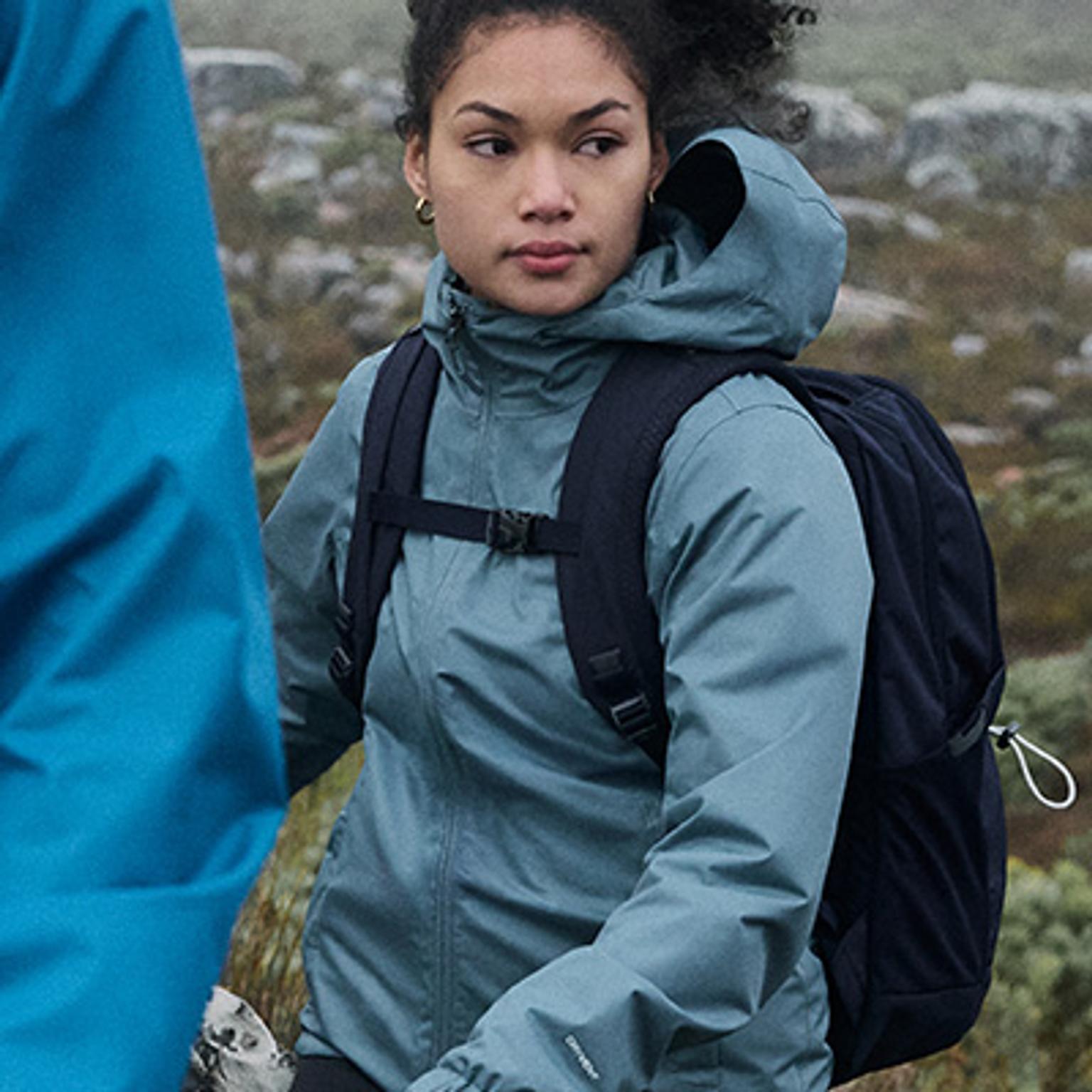 a woman wearing a blue jacket and a black backpack is walking in a field .