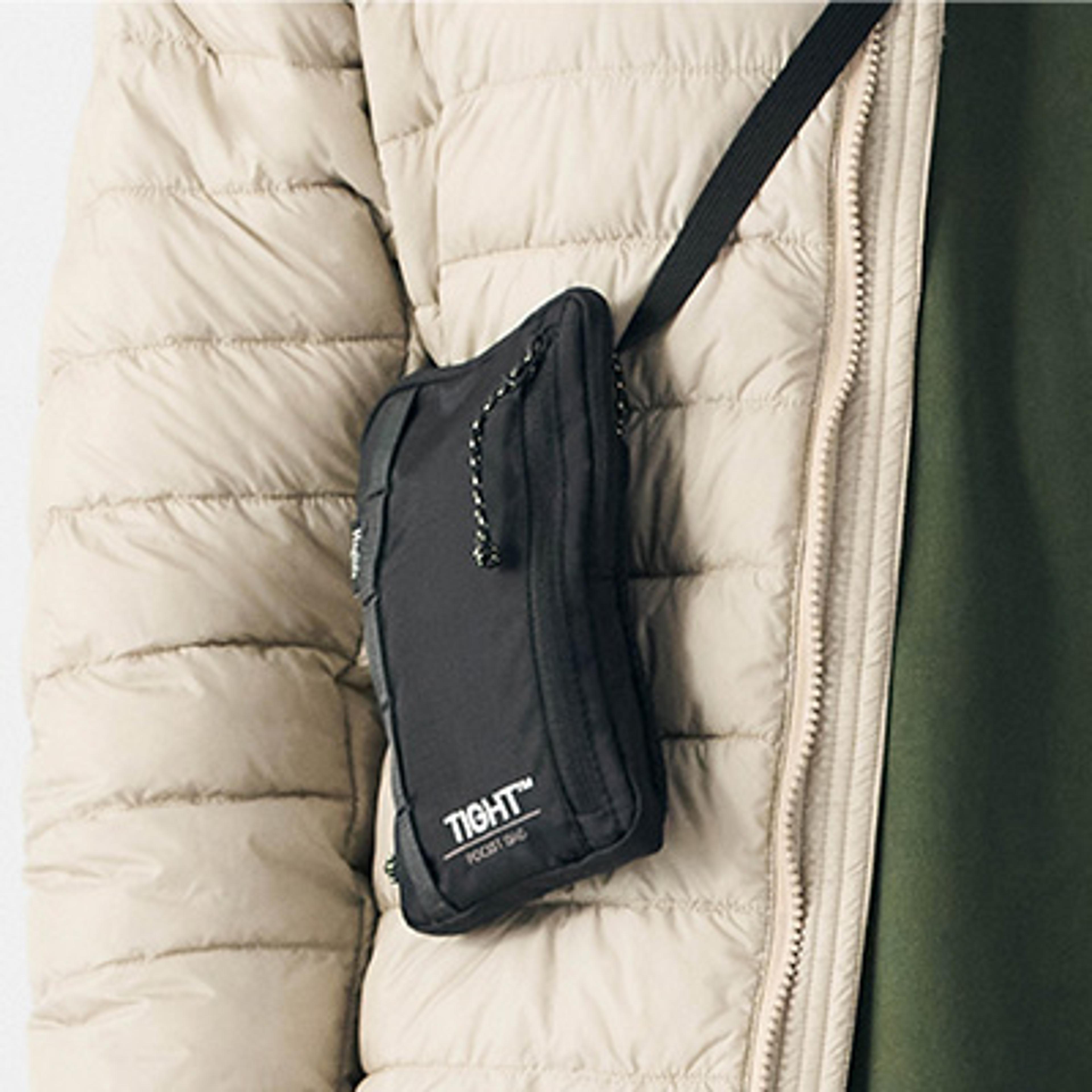 a person is wearing a black purse attached to their jacket .