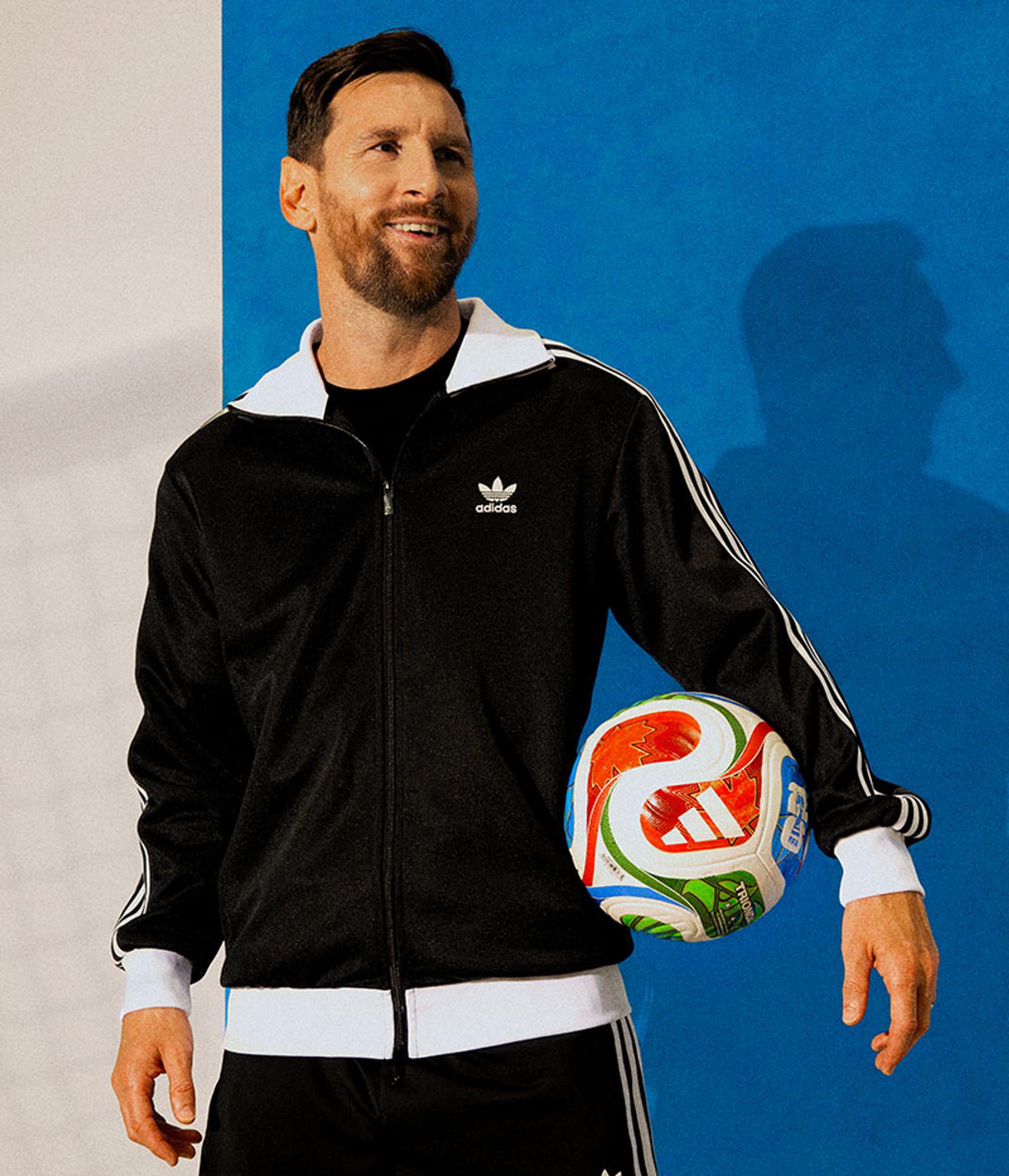 a man wearing a black adidas jacket is holding a soccer ball