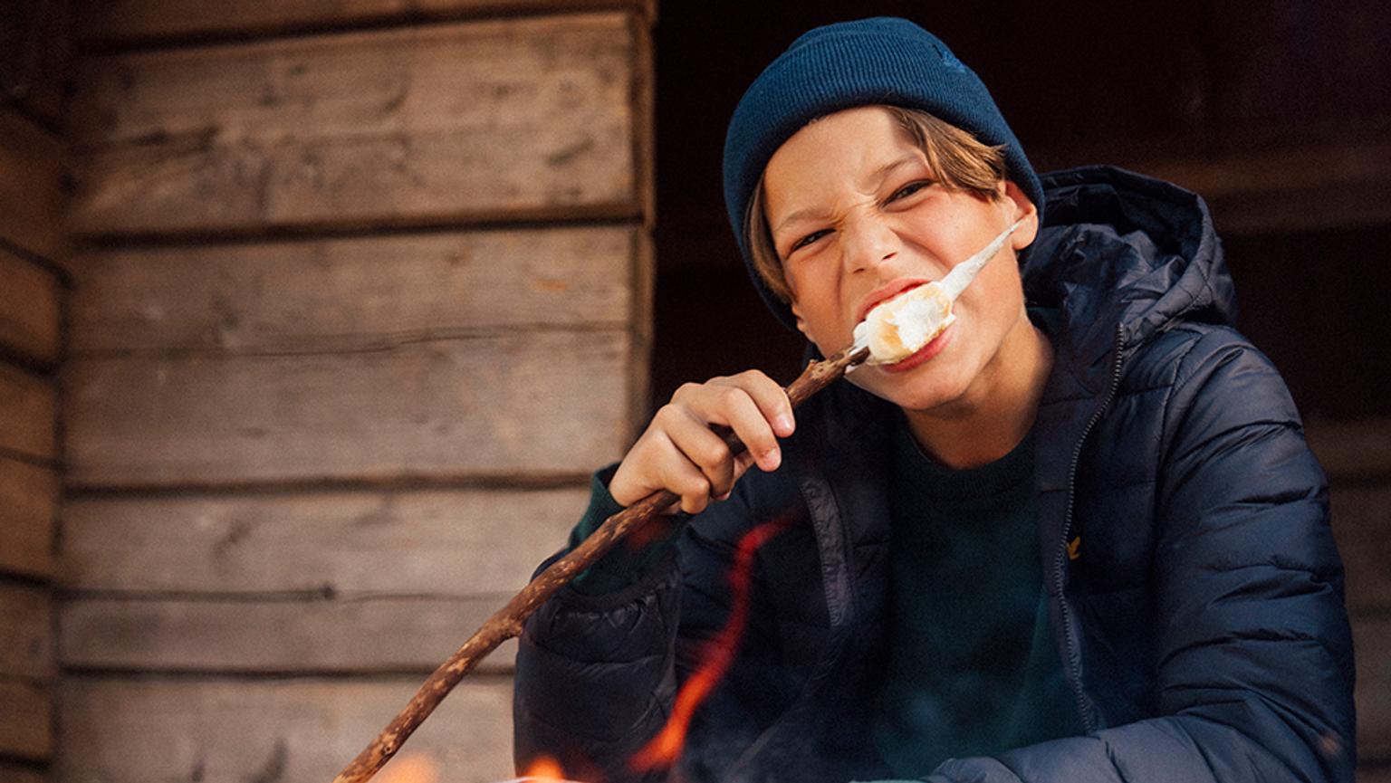 a young boy is eating a marshmallow on a stick over a fire .