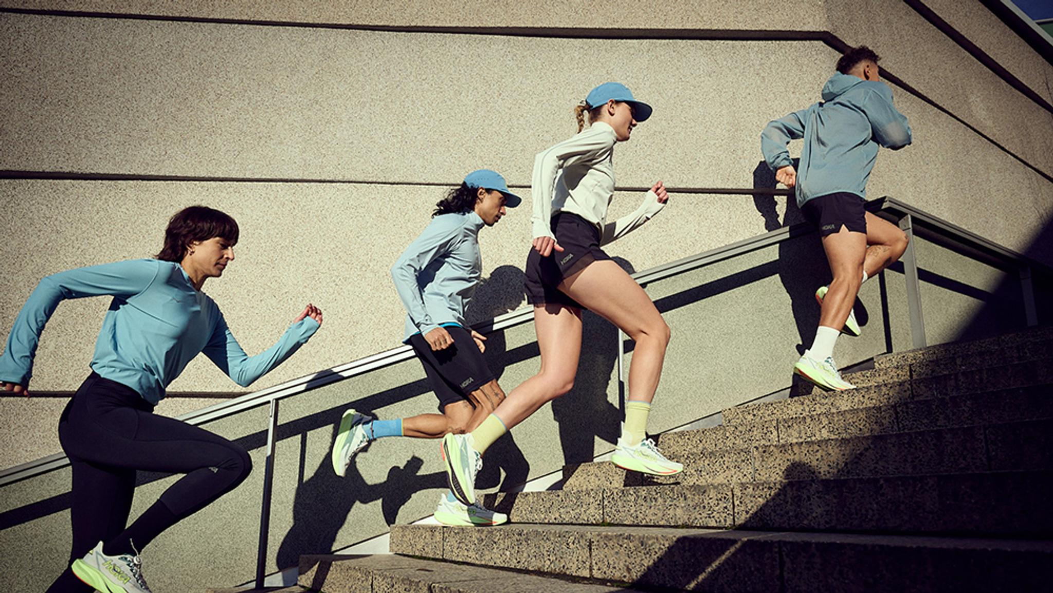 Four people in running shoes and athletic wear running up an outdoor concrete staircase.