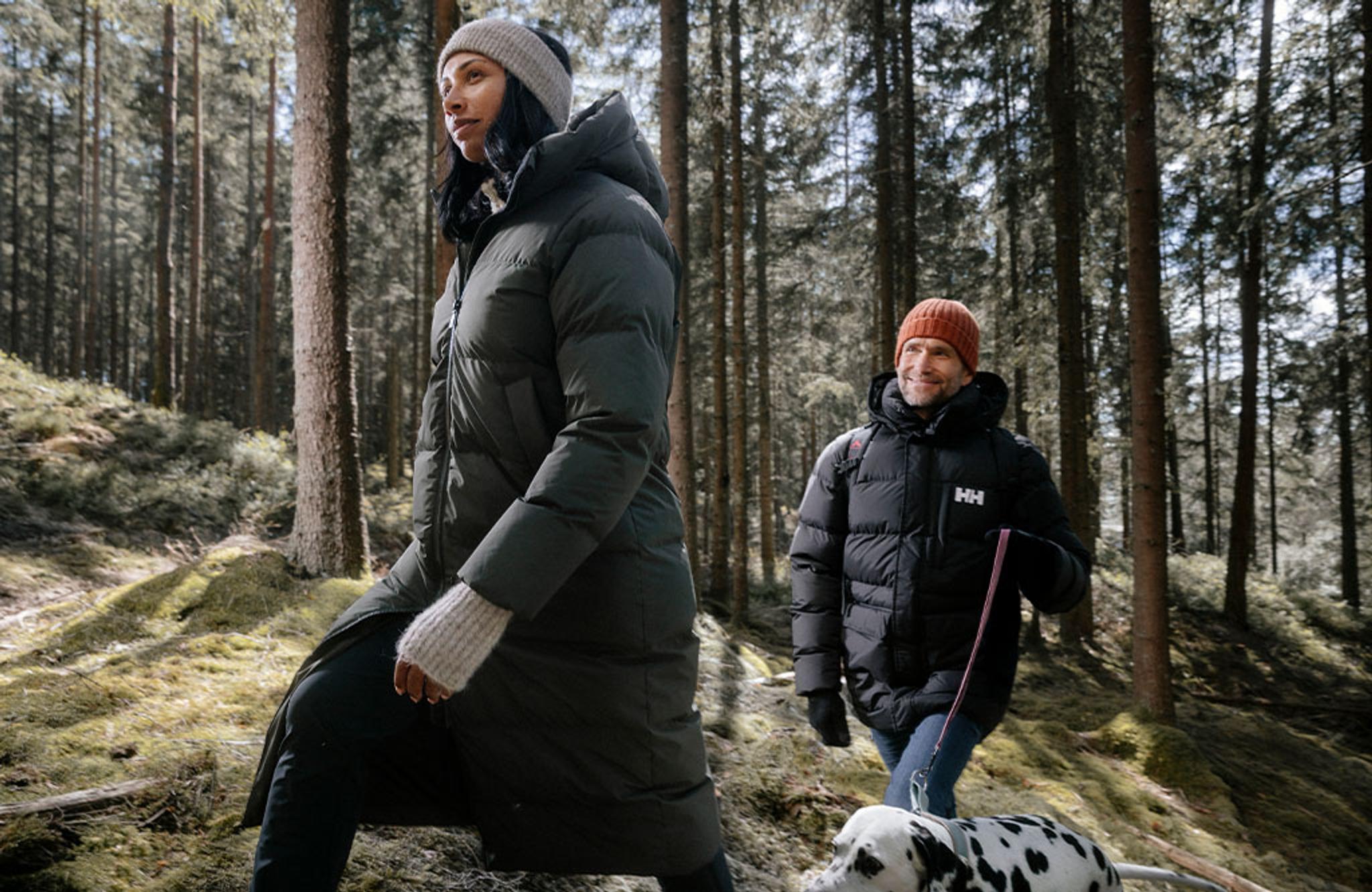 a man and a woman are walking a dalmatian dog through the woods .