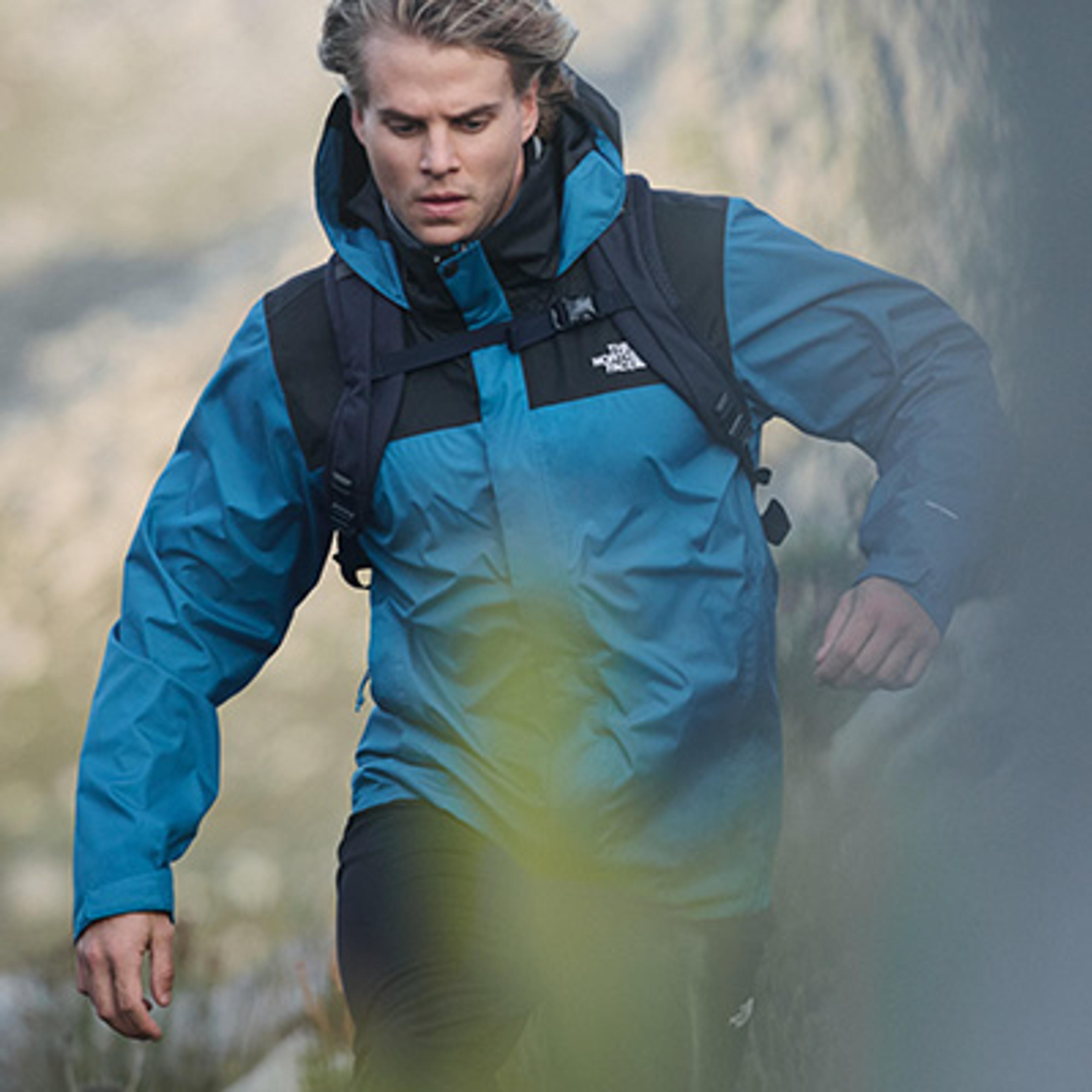 a man wearing a blue jacket and a backpack is walking through a forest .