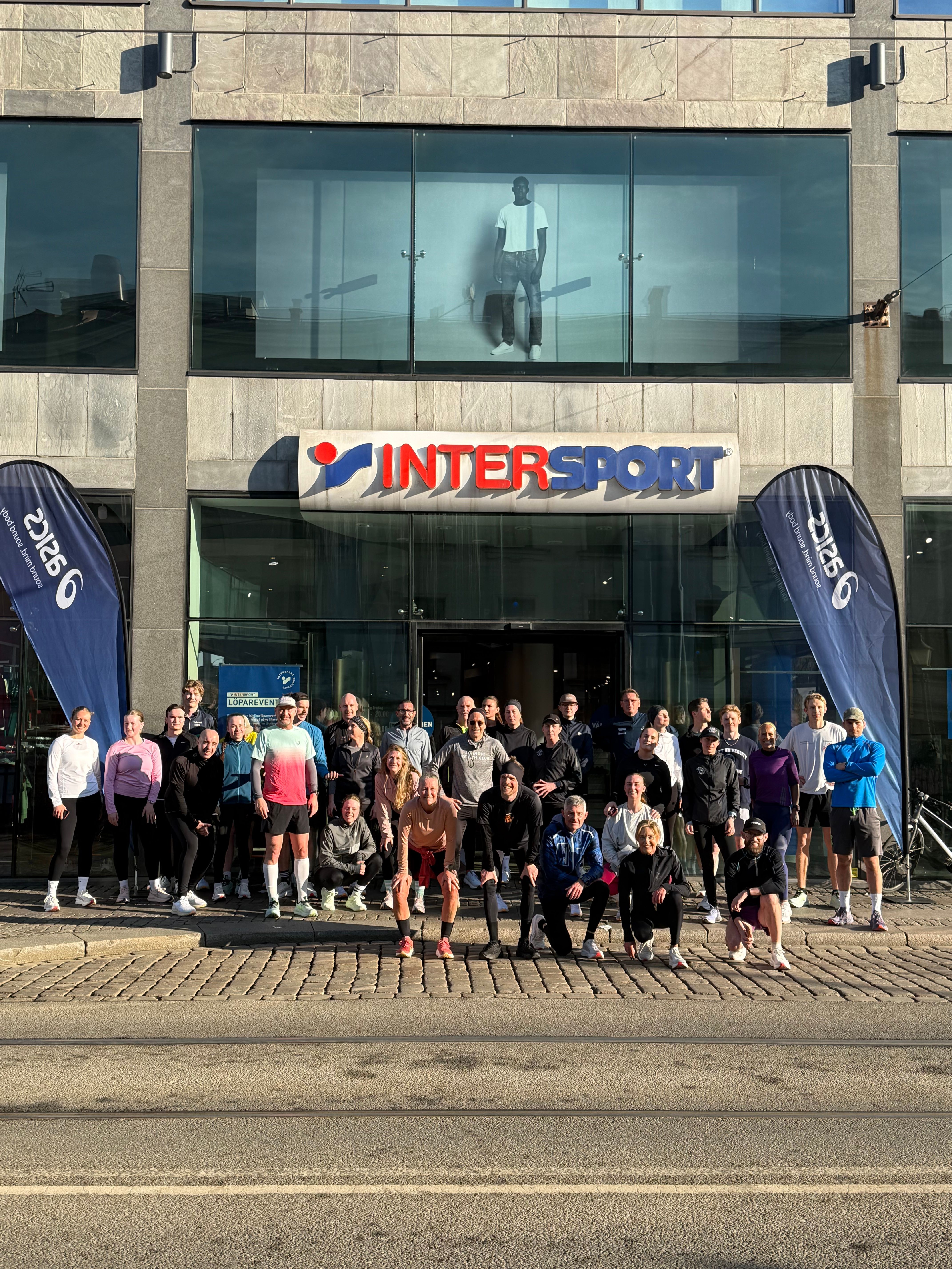 A group of people in athletic wear pose for a photo in front of an Intersport store.
