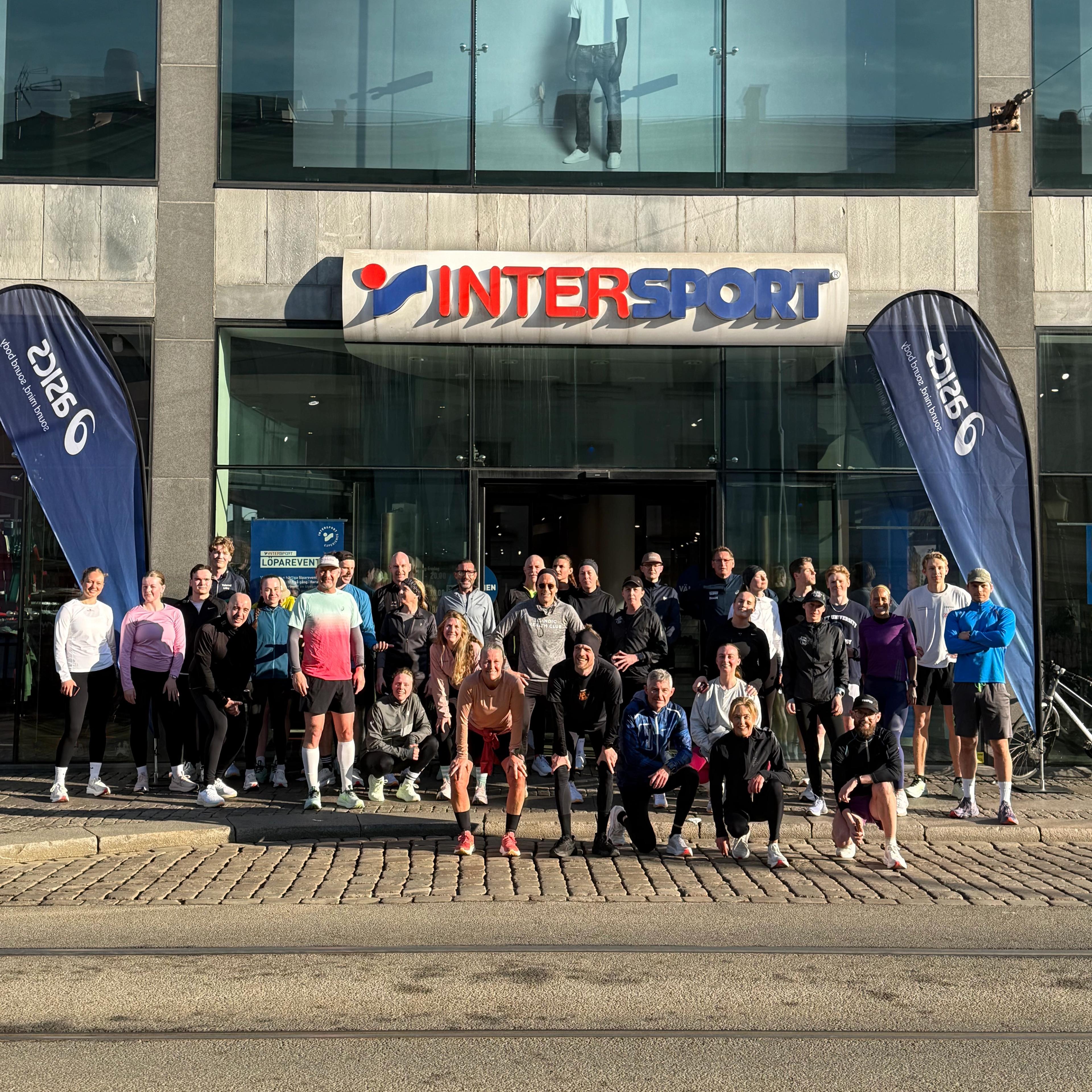A group of people in athletic wear pose for a photo in front of an Intersport store.