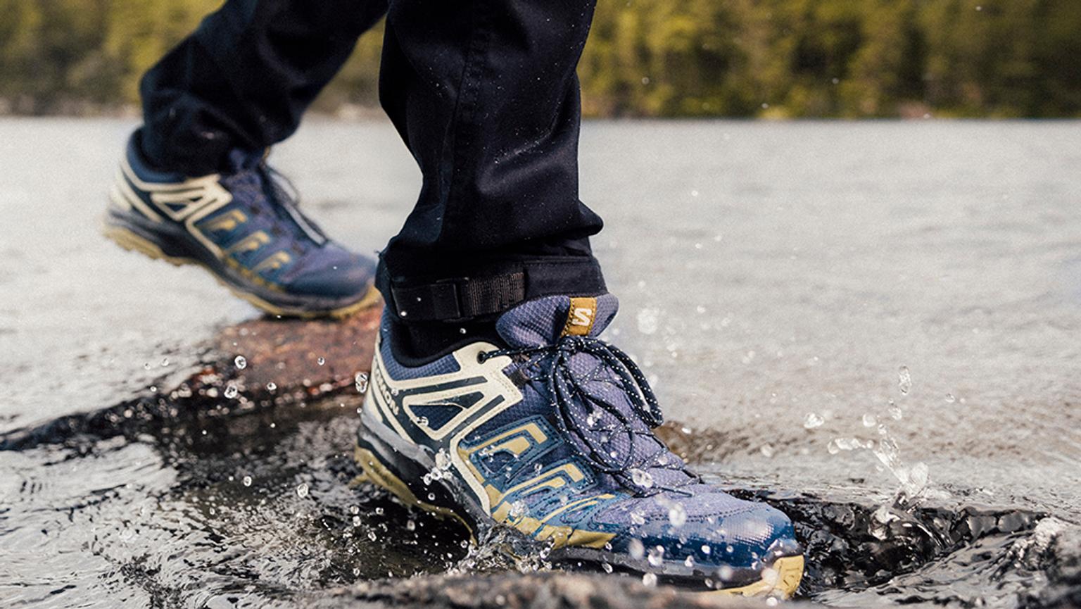 a person wearing a pair of salomon shoes is walking through a puddle of water .