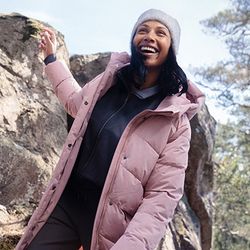 a woman wearing a pink jacket and a hat is standing on a rock .