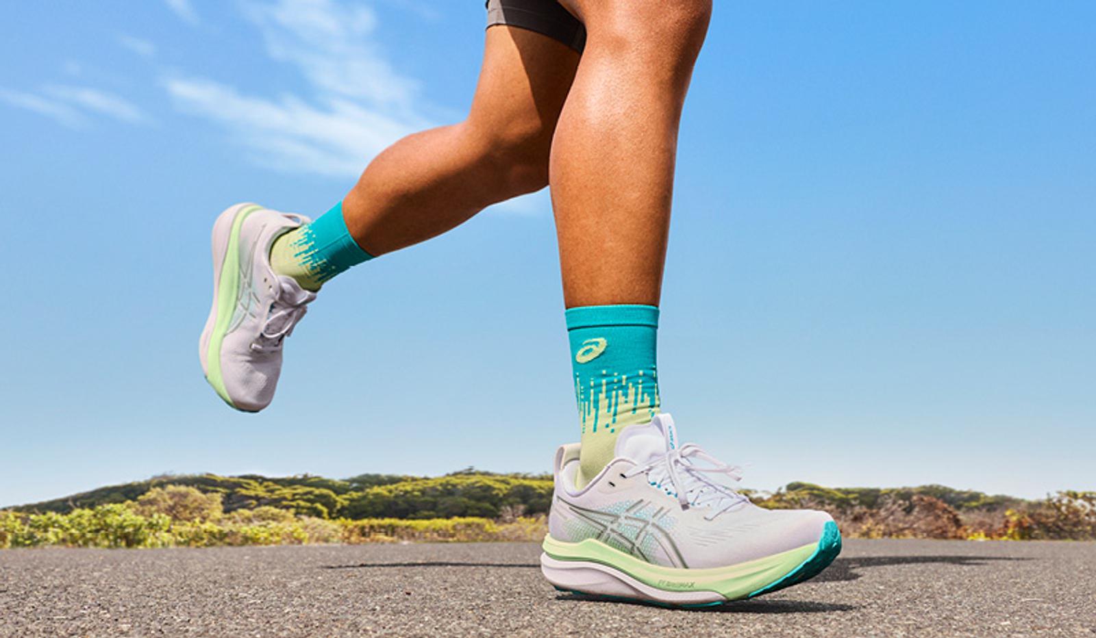 A runner's legs in white ASICS shoes and vibrant teal and lime green socks on a paved road.