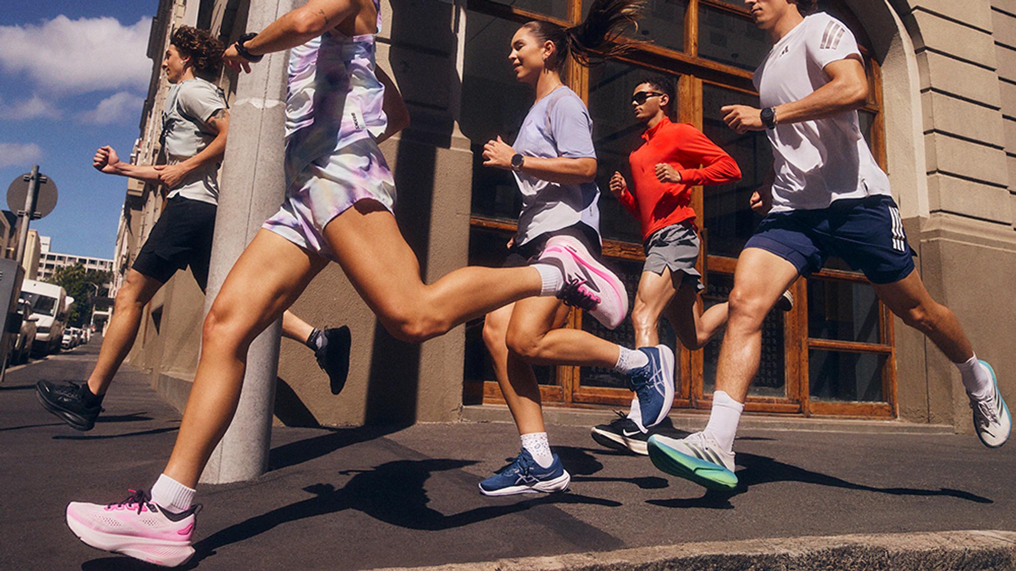 Five people running on a city sidewalk in athletic apparel and running shoes.