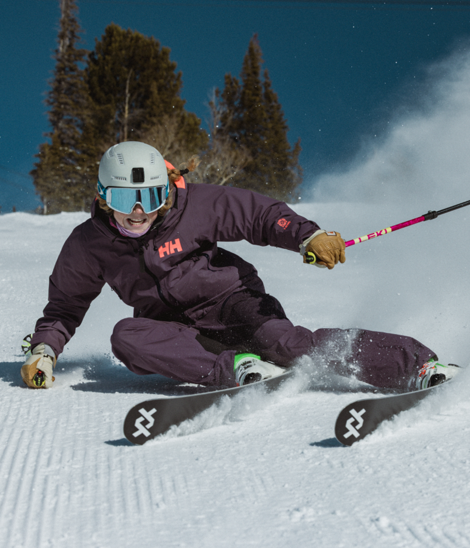 A skier in a purple suit carves a turn on a snowy mountain, kicking up snow.