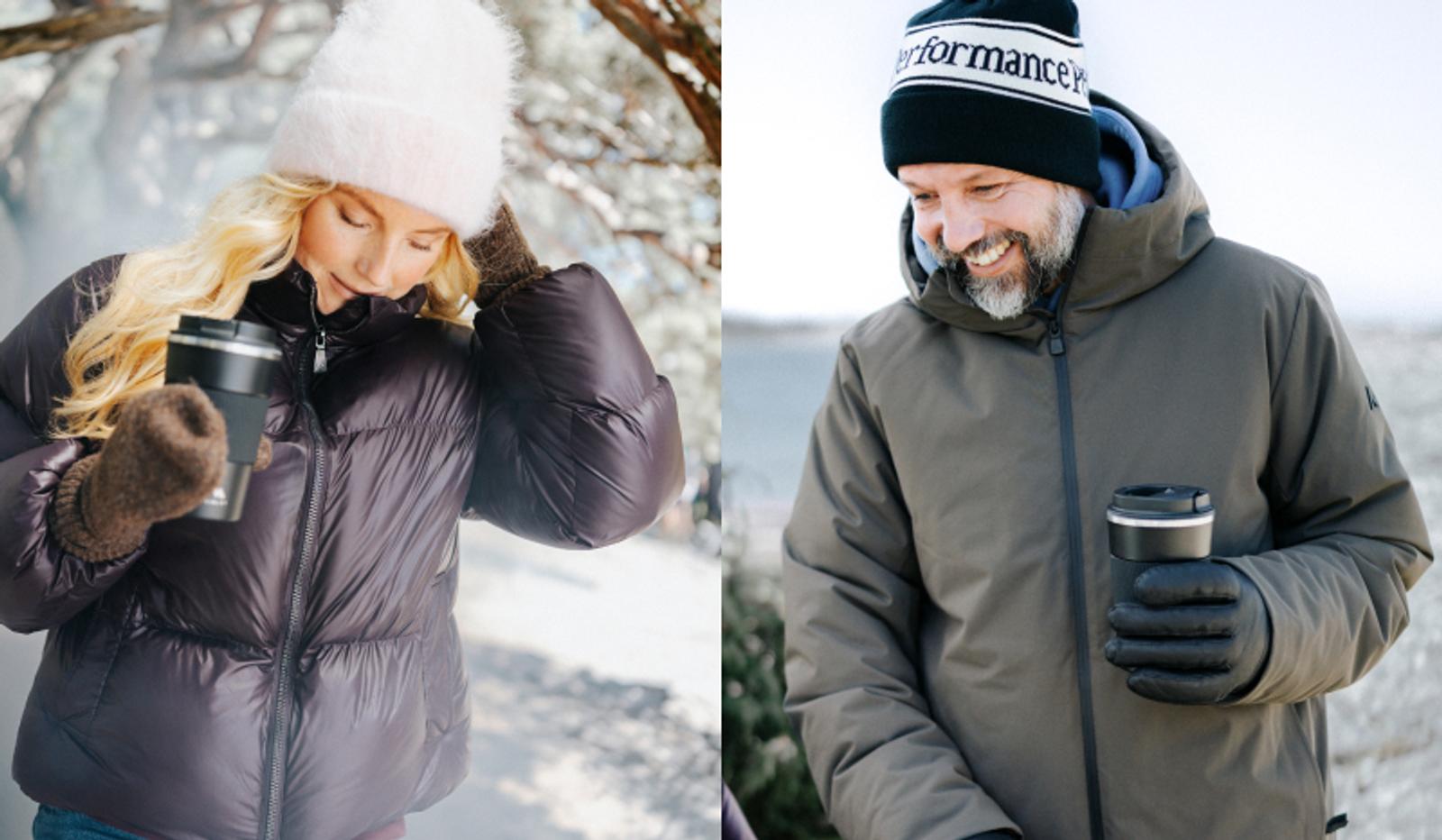 Two people in winter clothing, a woman and a man, each holding a thermal mug outdoors.