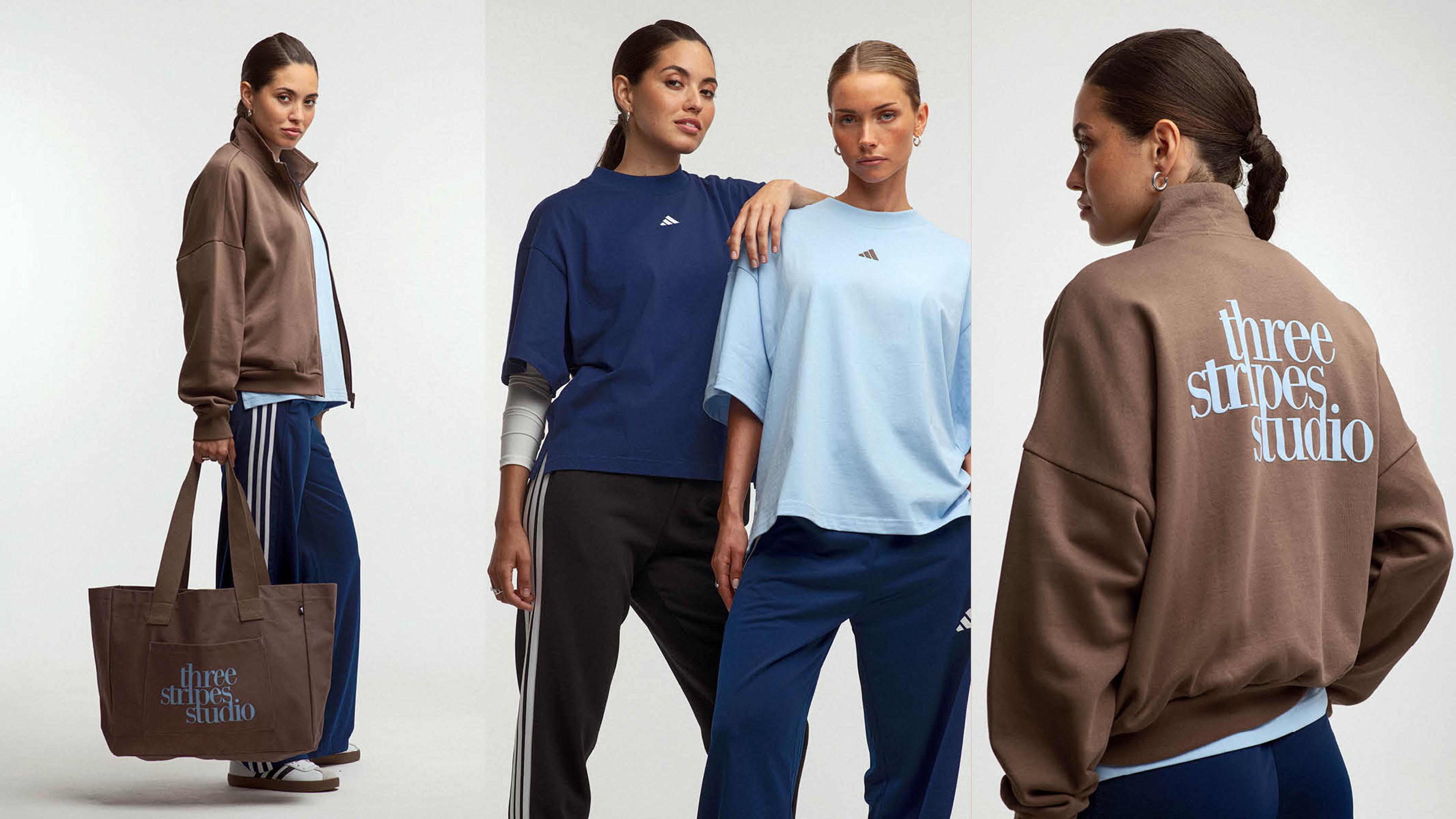 Three women model Adidas "Three Stripes Studio" activewear, featuring brown jackets, blue t-shirts, track pants, and a matching tote bag.