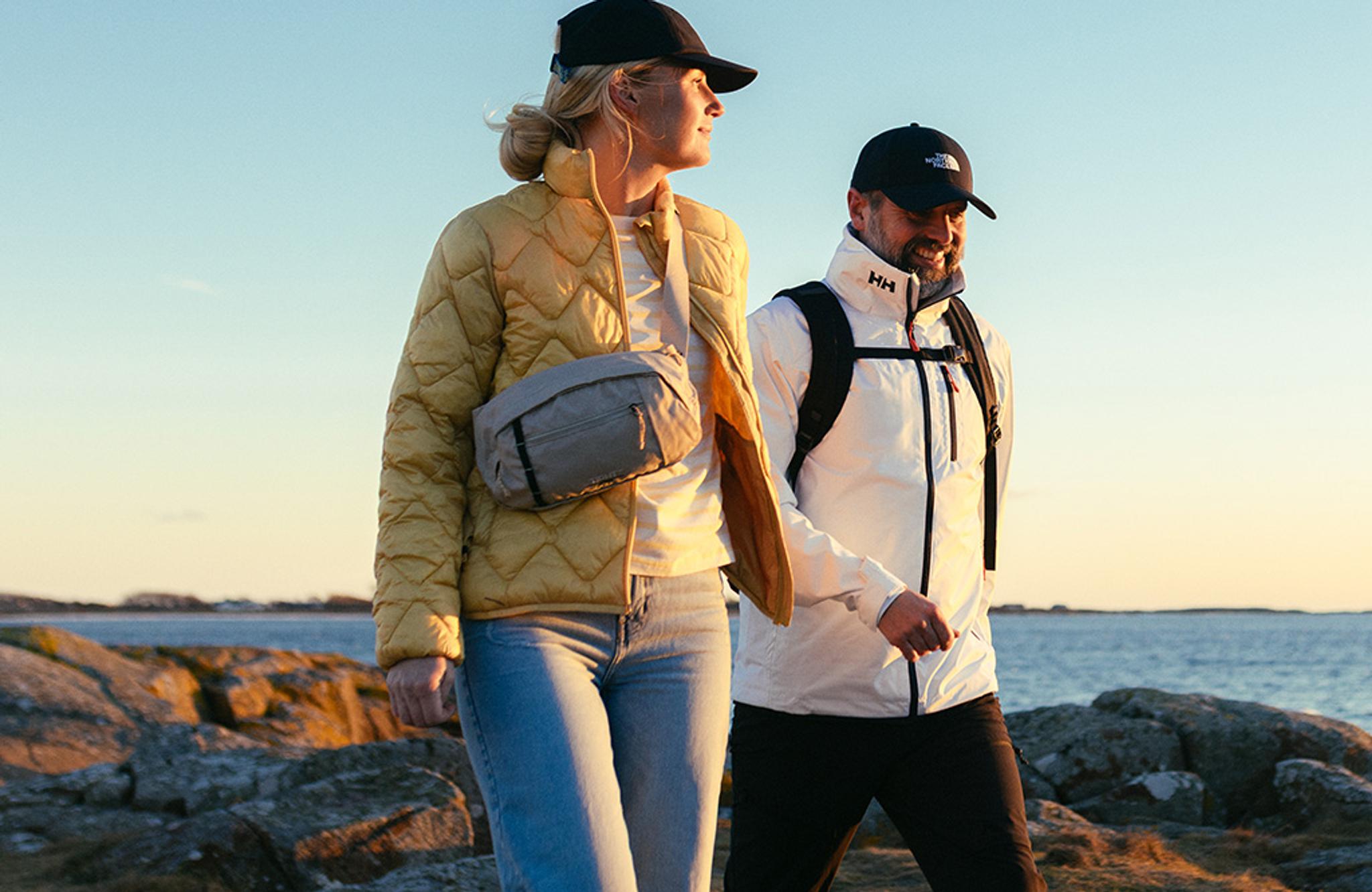 A man and woman in outdoor gear walking along a rocky coast at sunset.
