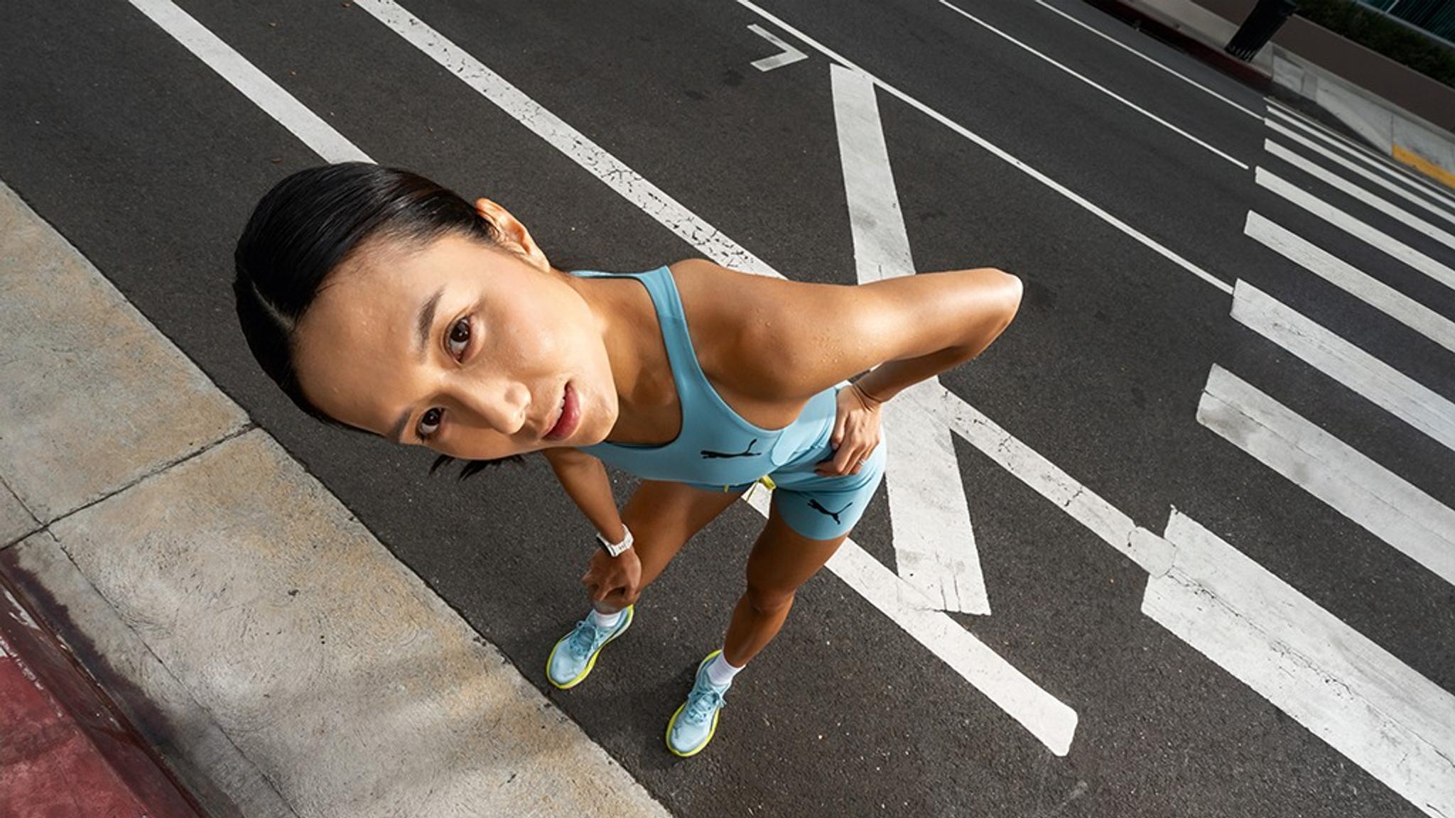 A woman in blue athletic wear looks up at the camera from a high angle, standing on a street with white markings.