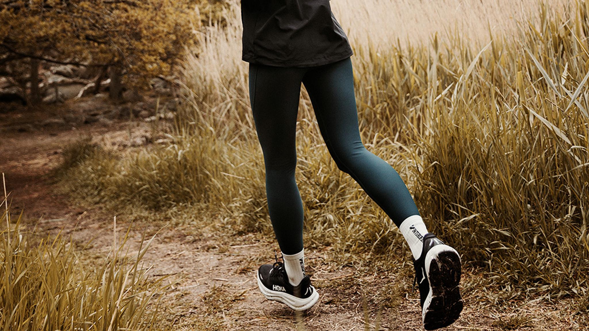 Runner's legs and feet on a dirt trail through tall golden grass.