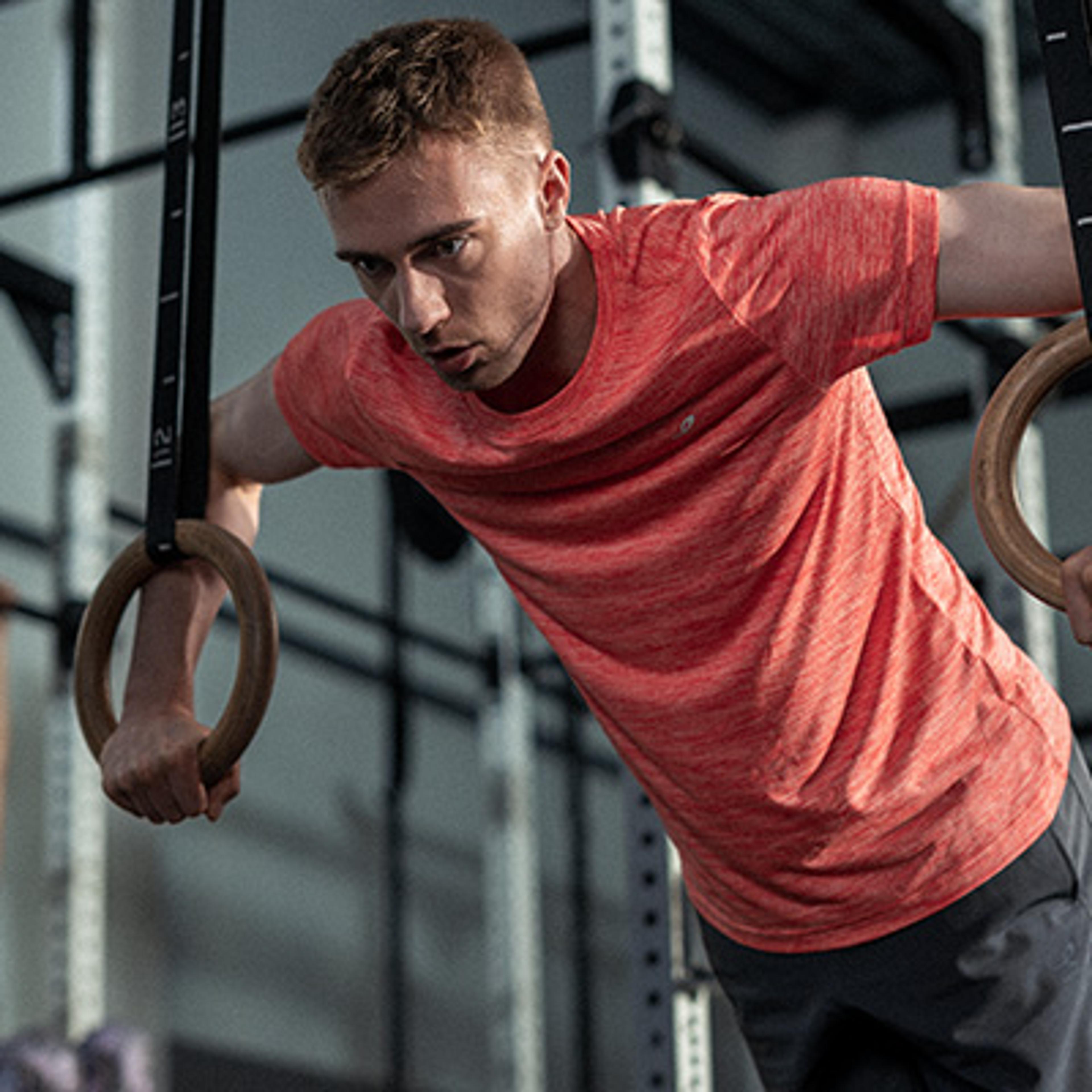 Focused man in a red t-shirt performing a dip on gymnastic rings.