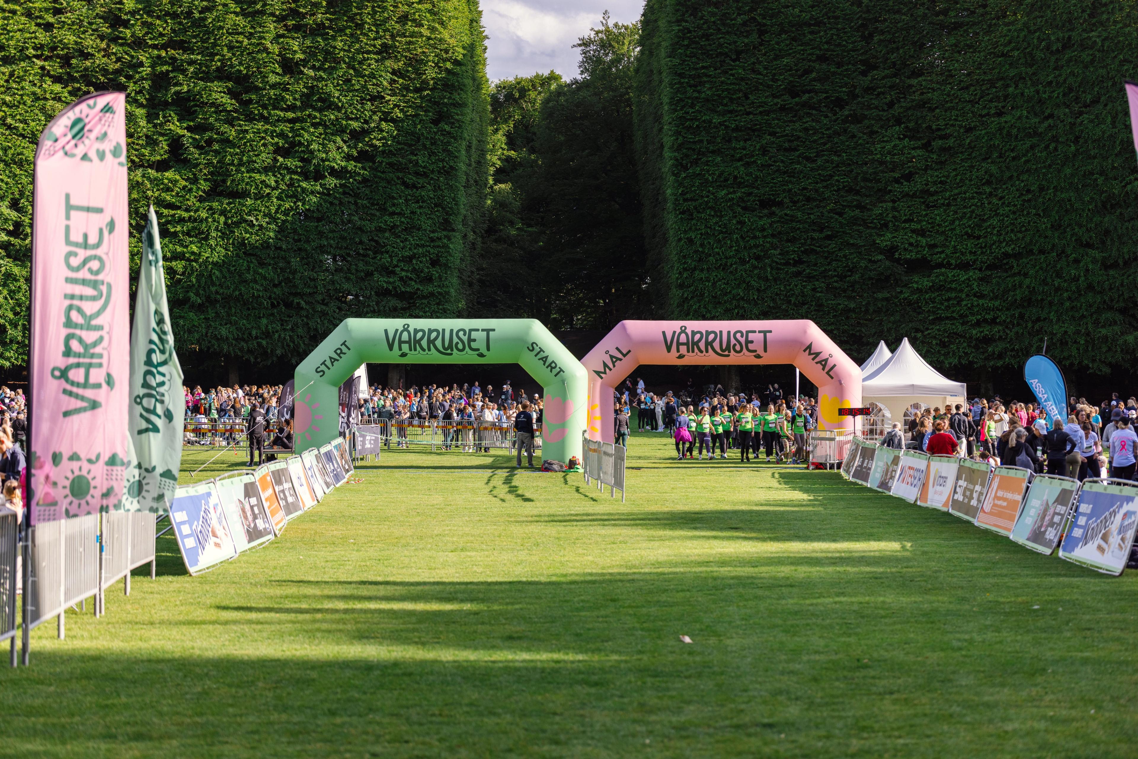 People gathered at the Vårruset race event with green start and pink finish arches on a grassy field.