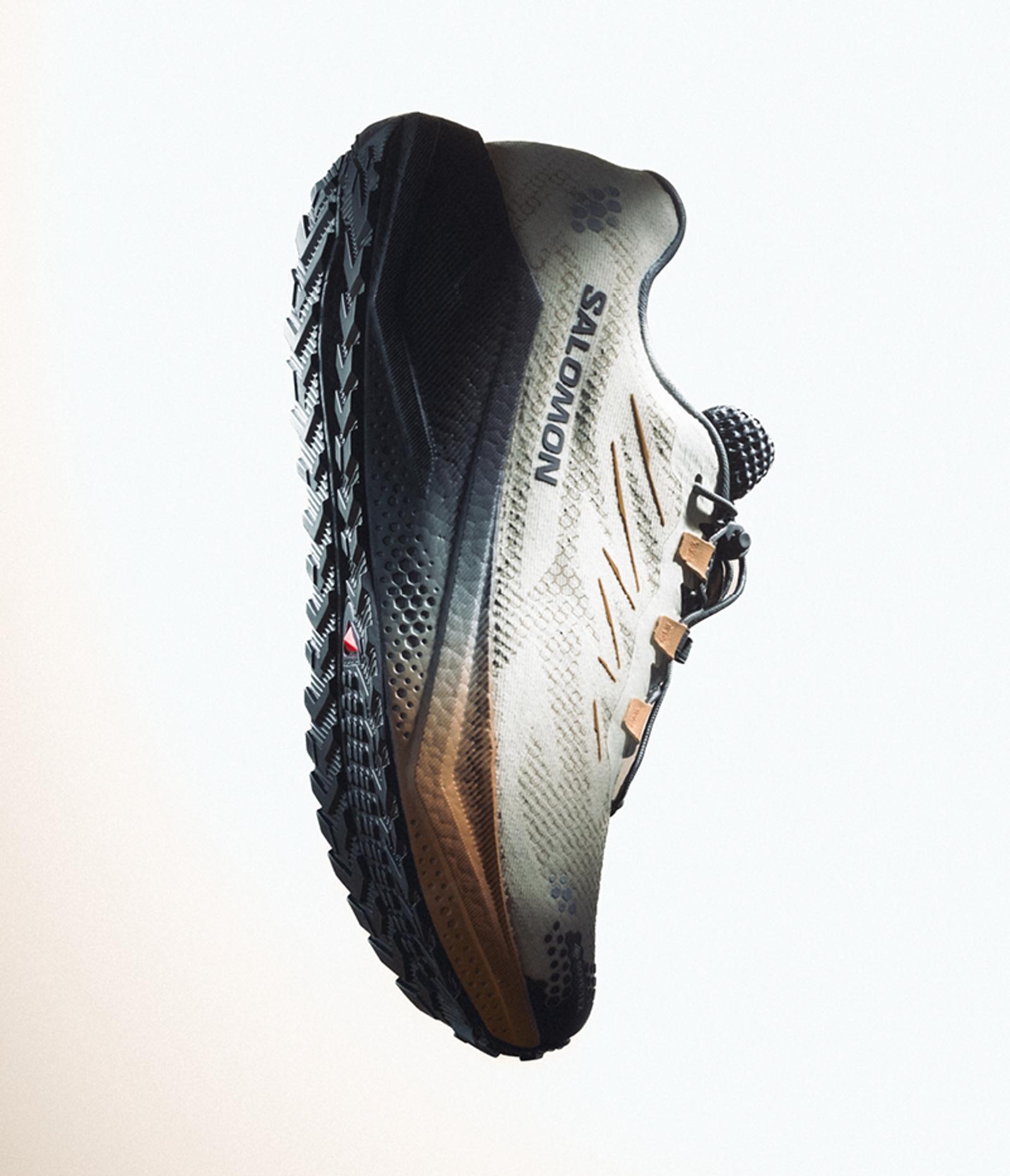 A Salomon trail running shoe with a light gray upper, black sole, and bronze accents, angled on a white background.