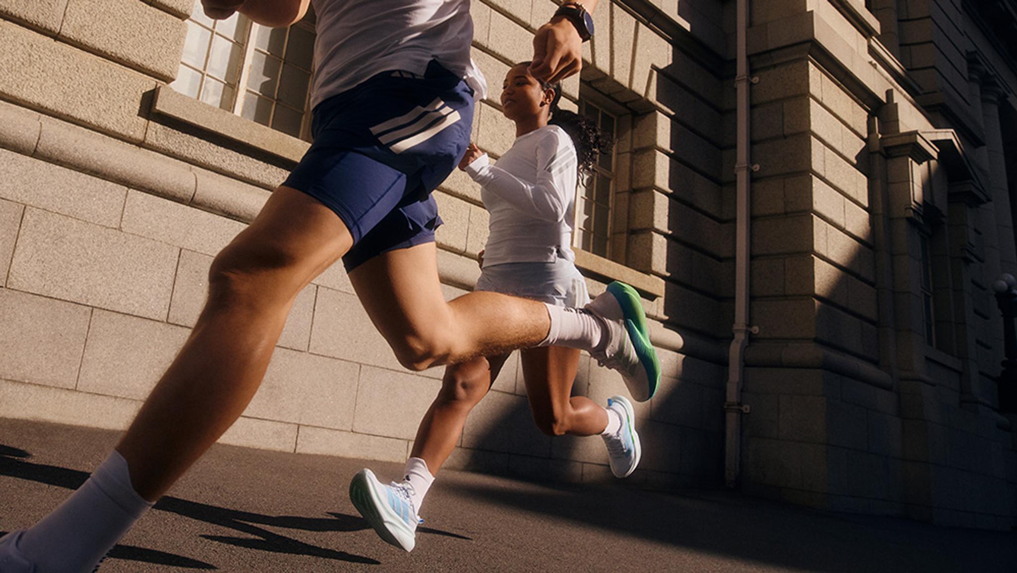 Two people running past a stone building, wearing white running shoes