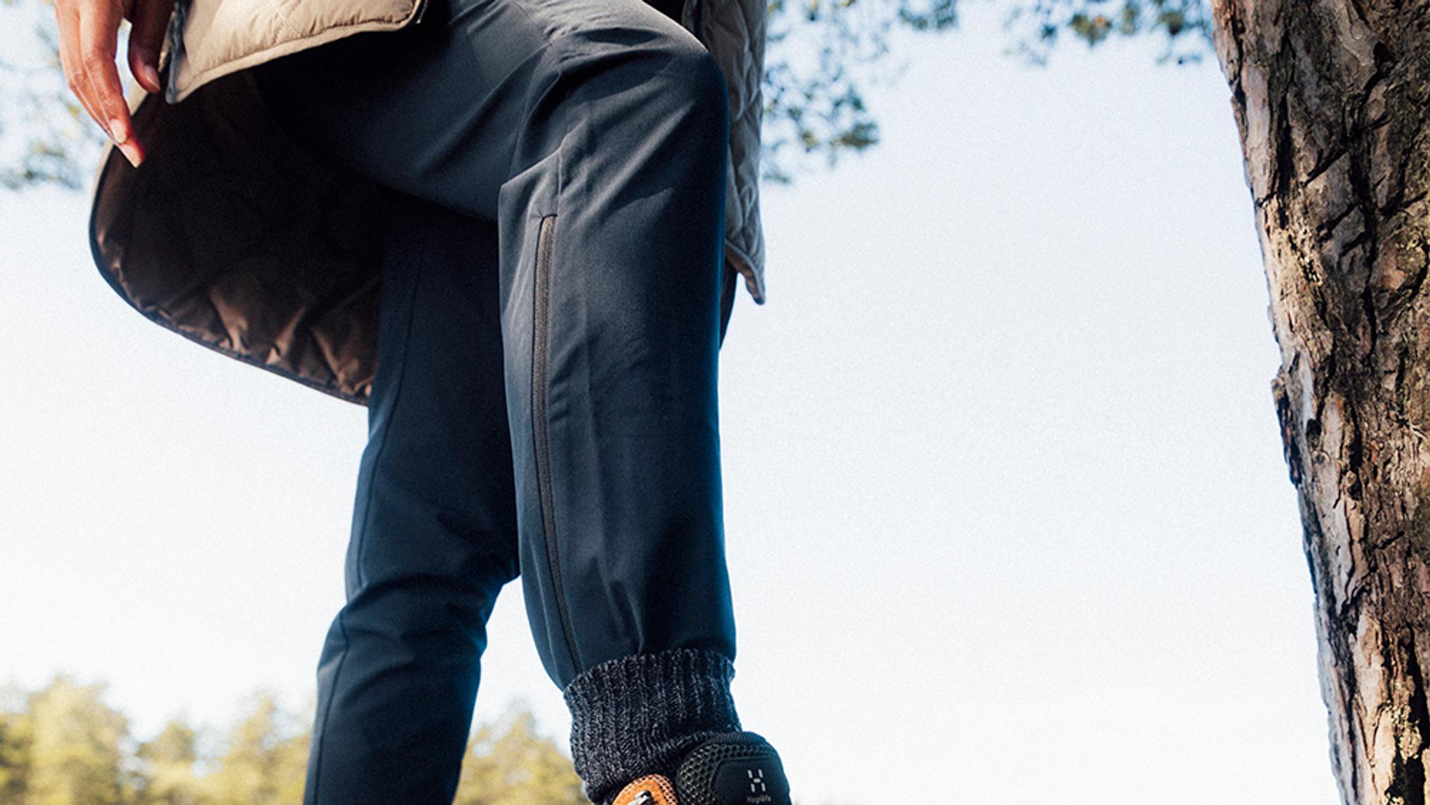 a woman is climbing a tree wearing new outdoor pants and a jacket .