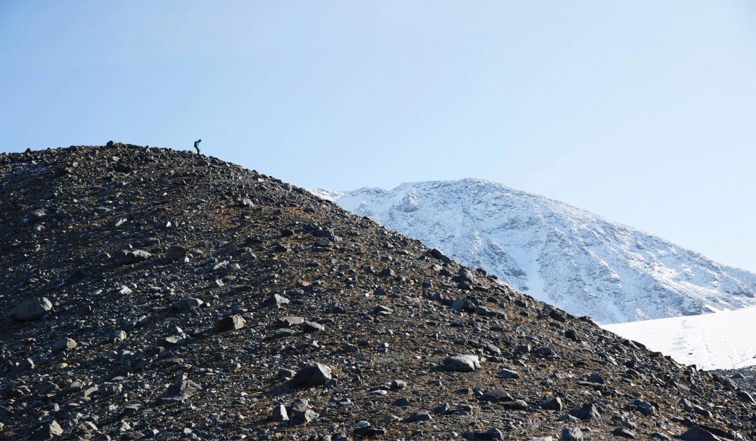 a person is standing on top of a rocky hill with a snowy mountain in the background .