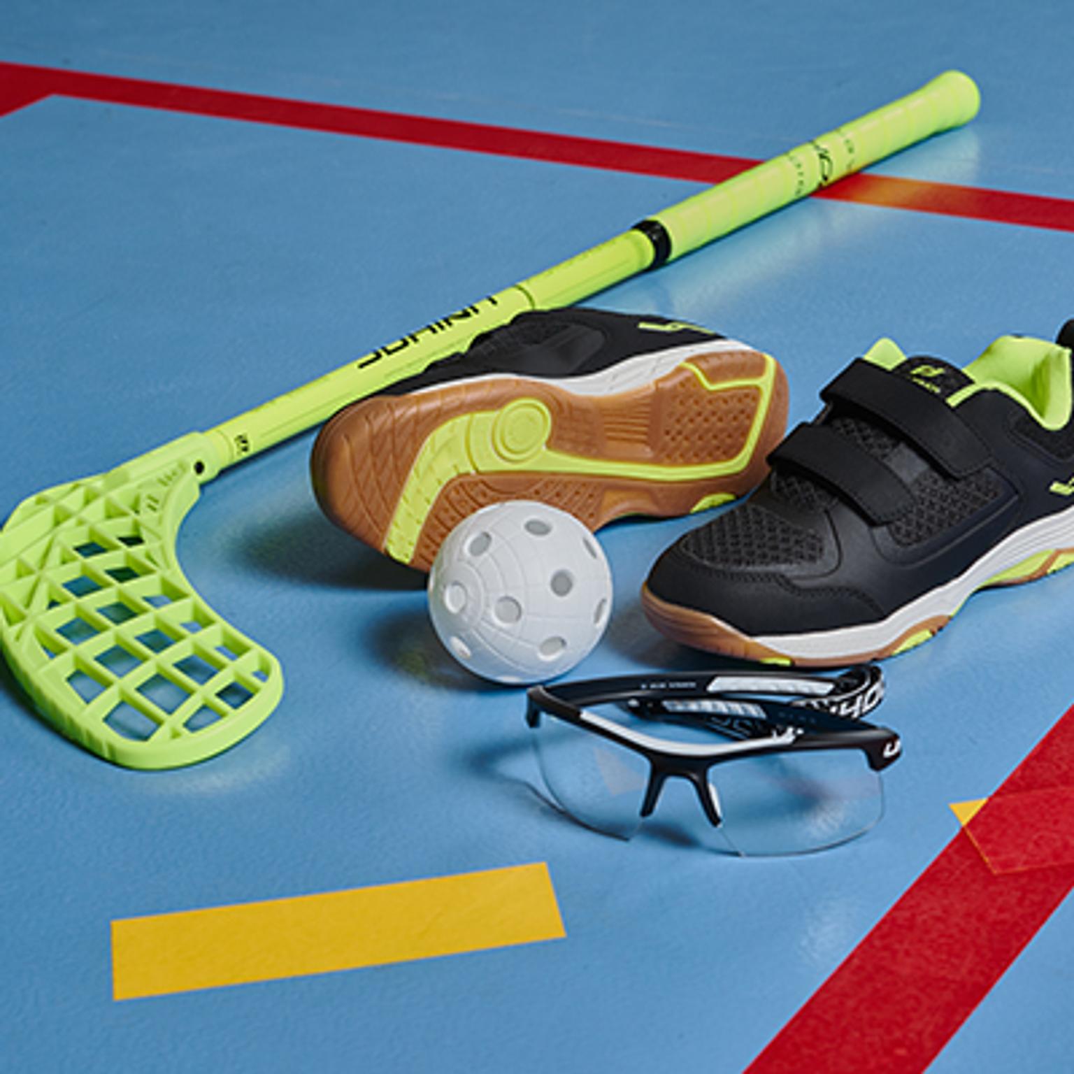 a floorball stick , shoes , glasses , and a ball are on a blue floor .