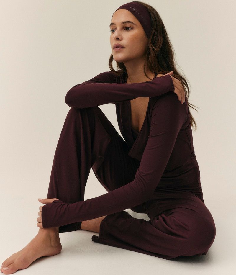 A woman sits on the floor wearing a dark plum loungewear set and matching headband.