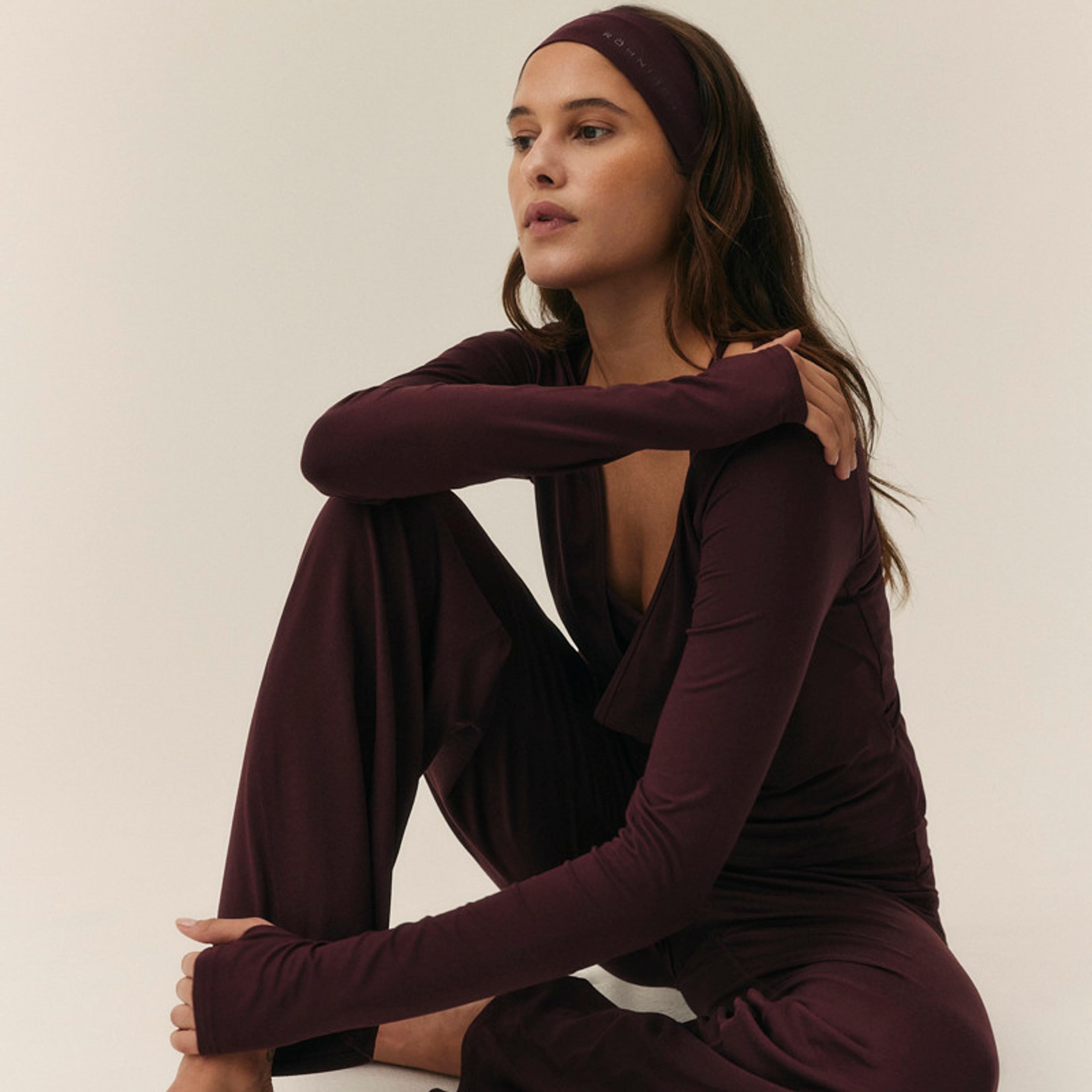 A woman sits on the floor wearing a dark plum loungewear set and matching headband.