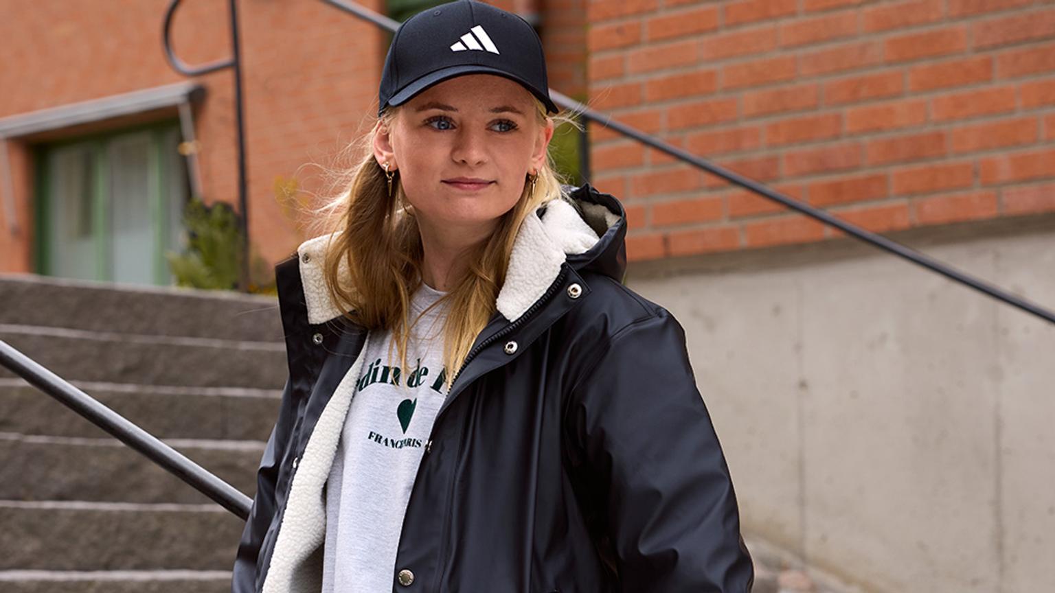 a woman wearing a black hat and a black jacket is standing on a set of stairs .