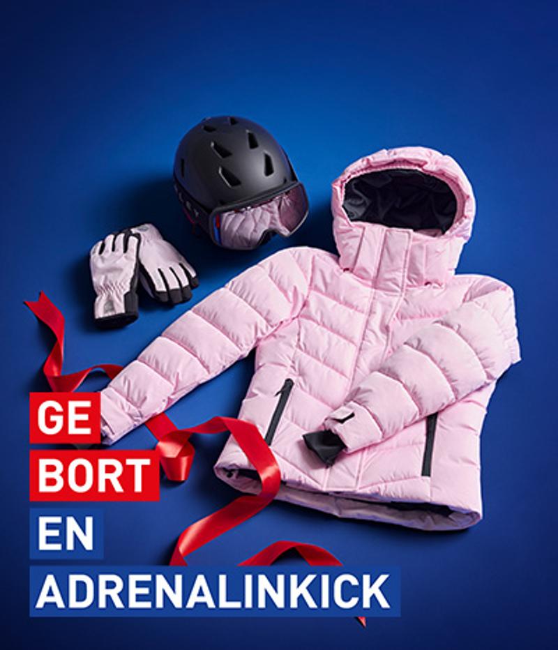 Pink ski jacket, gloves, and helmet with goggles on a blue background with a red ribbon and the text 'GEBORT EN ADRENALINKICK'.