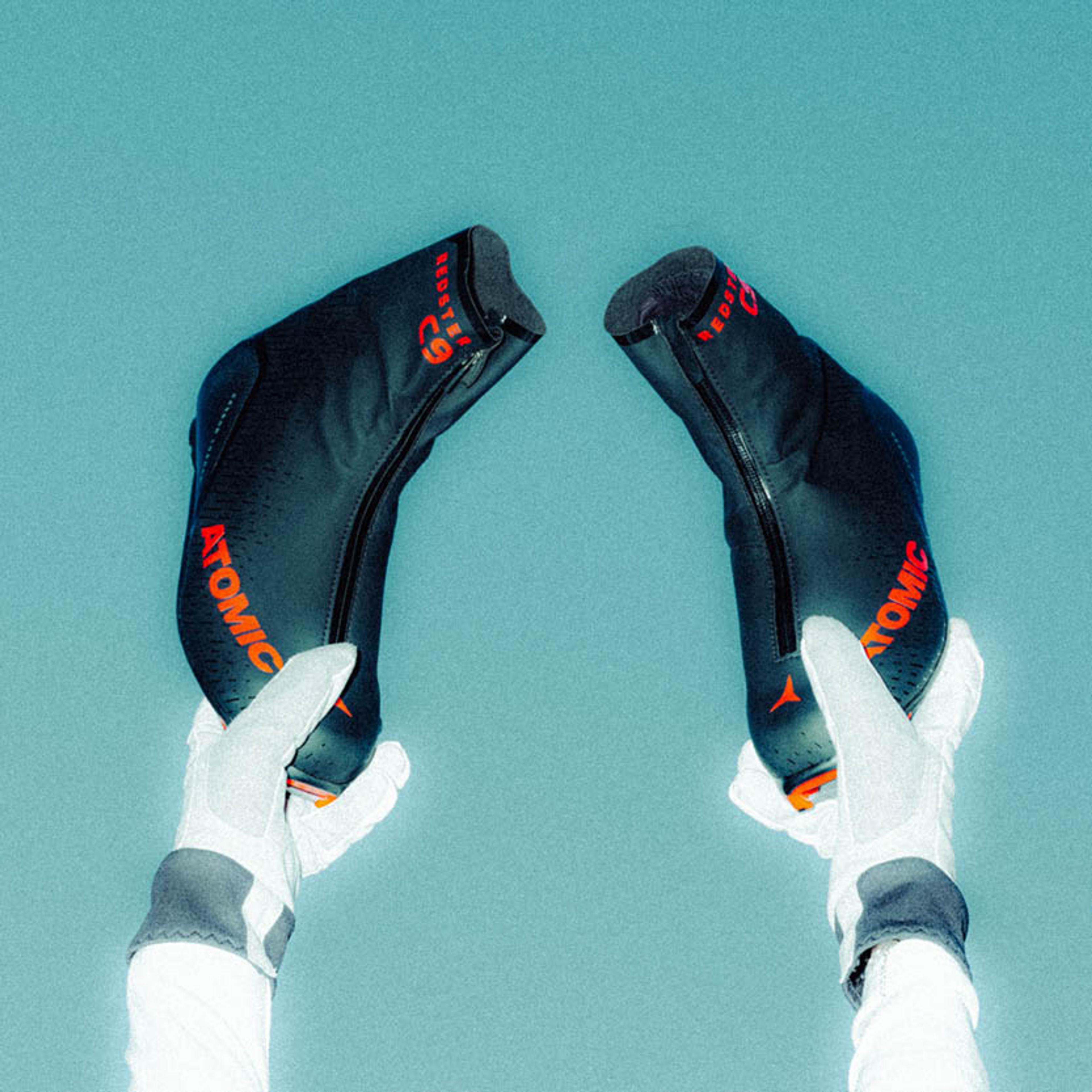 Two gloved hands hold up black Atomic Redster C9 ski boot liners against a light blue background.