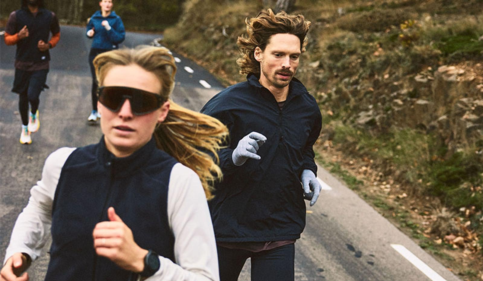 Group of runners on an uphill paved road, with a woman in sunglasses and a man in the foreground.