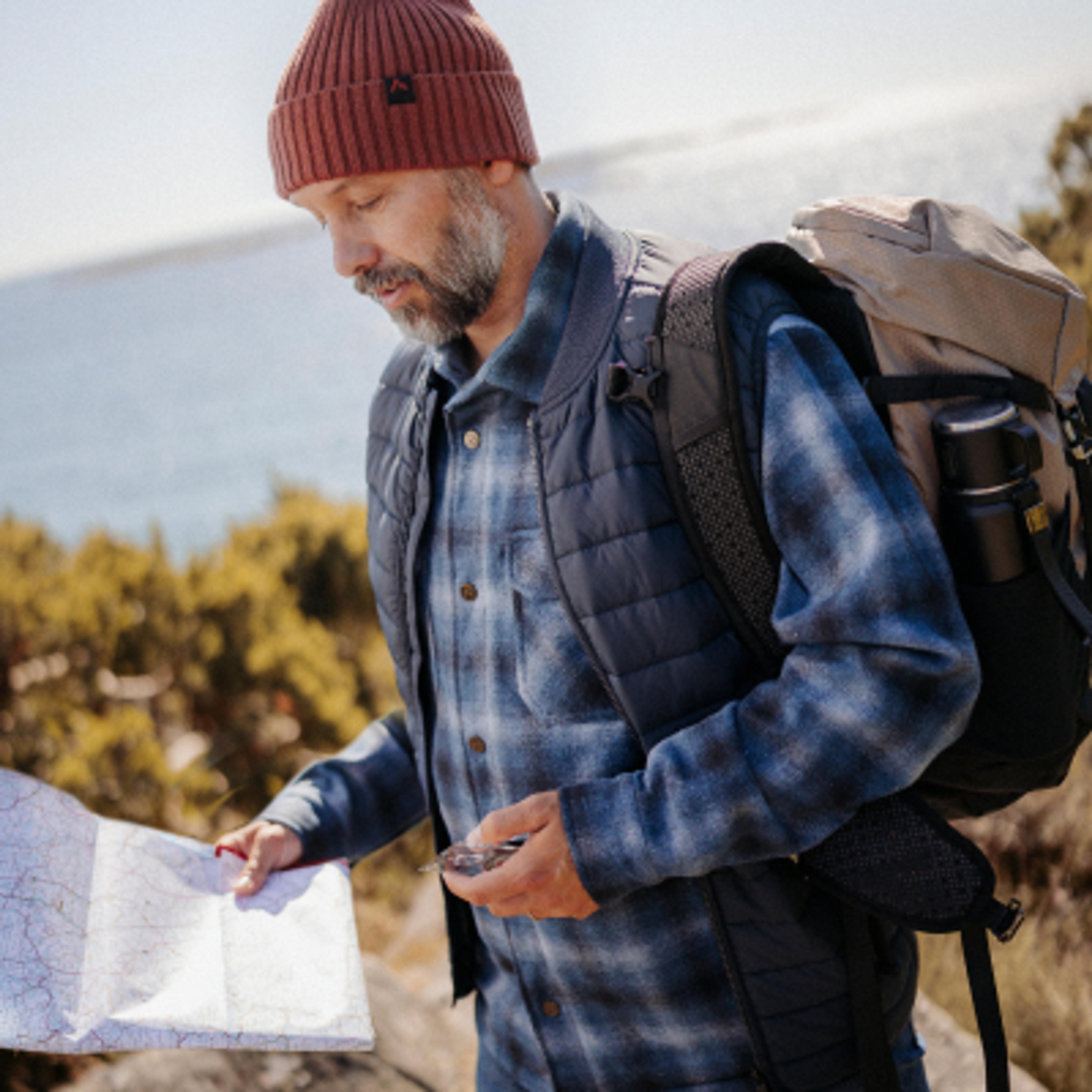 Man in a beanie looking at a map and compass while hiking.