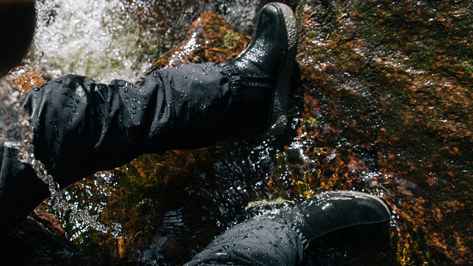 a kid wearing black boots is standing on a rock in the water .