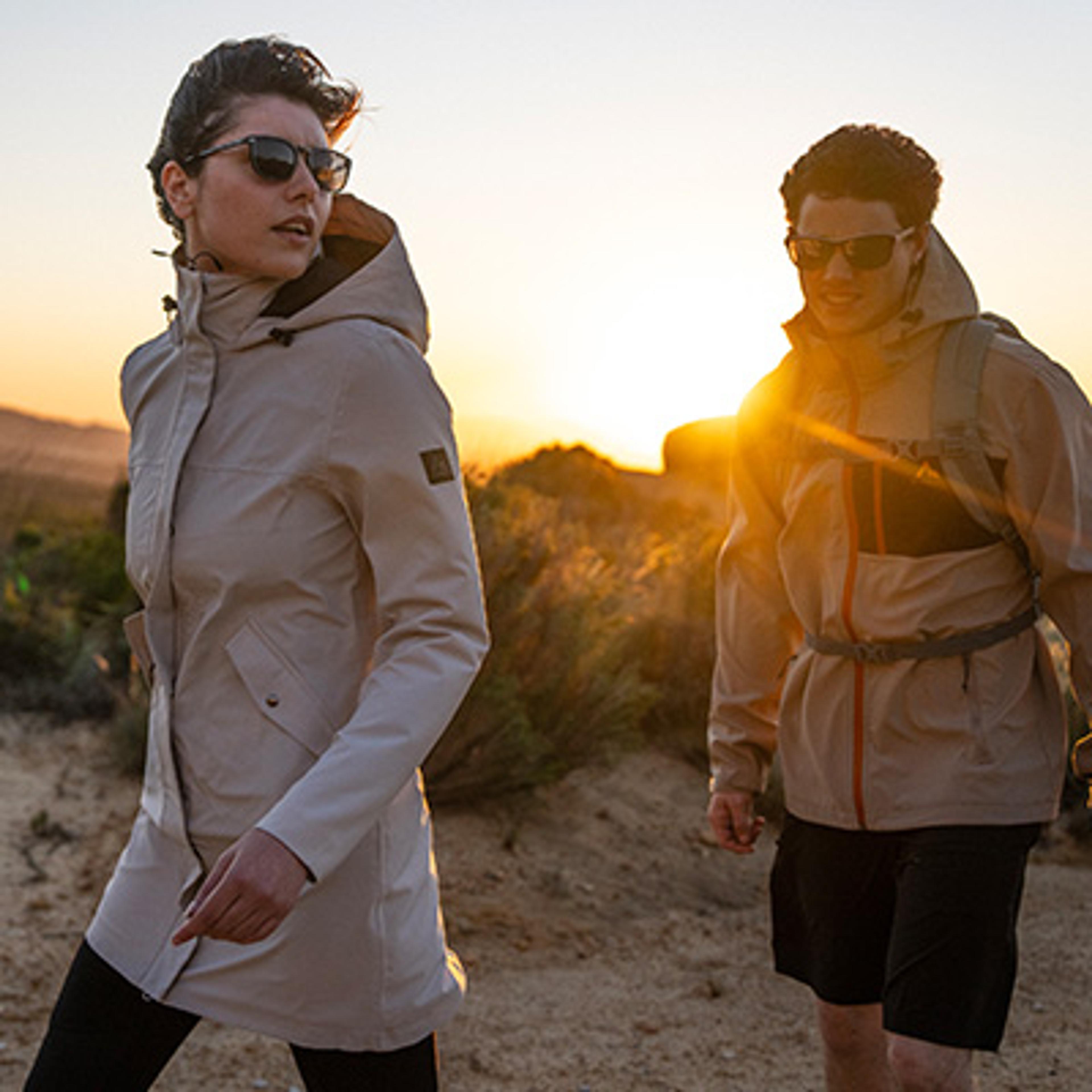 Two people hiking in outdoor jackets and sunglasses at sunset.
