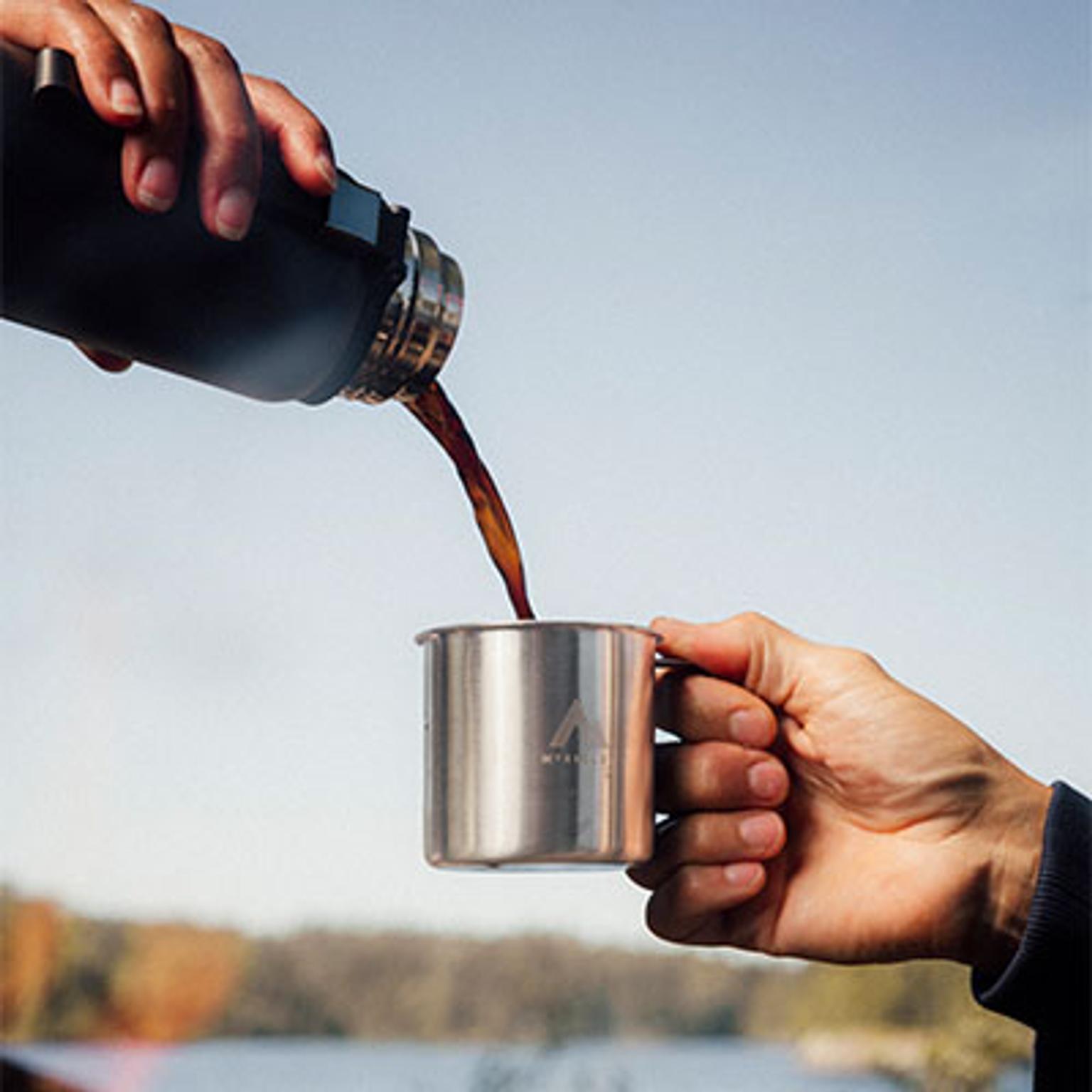 a person is pouring coffee into a stainless steel mug .