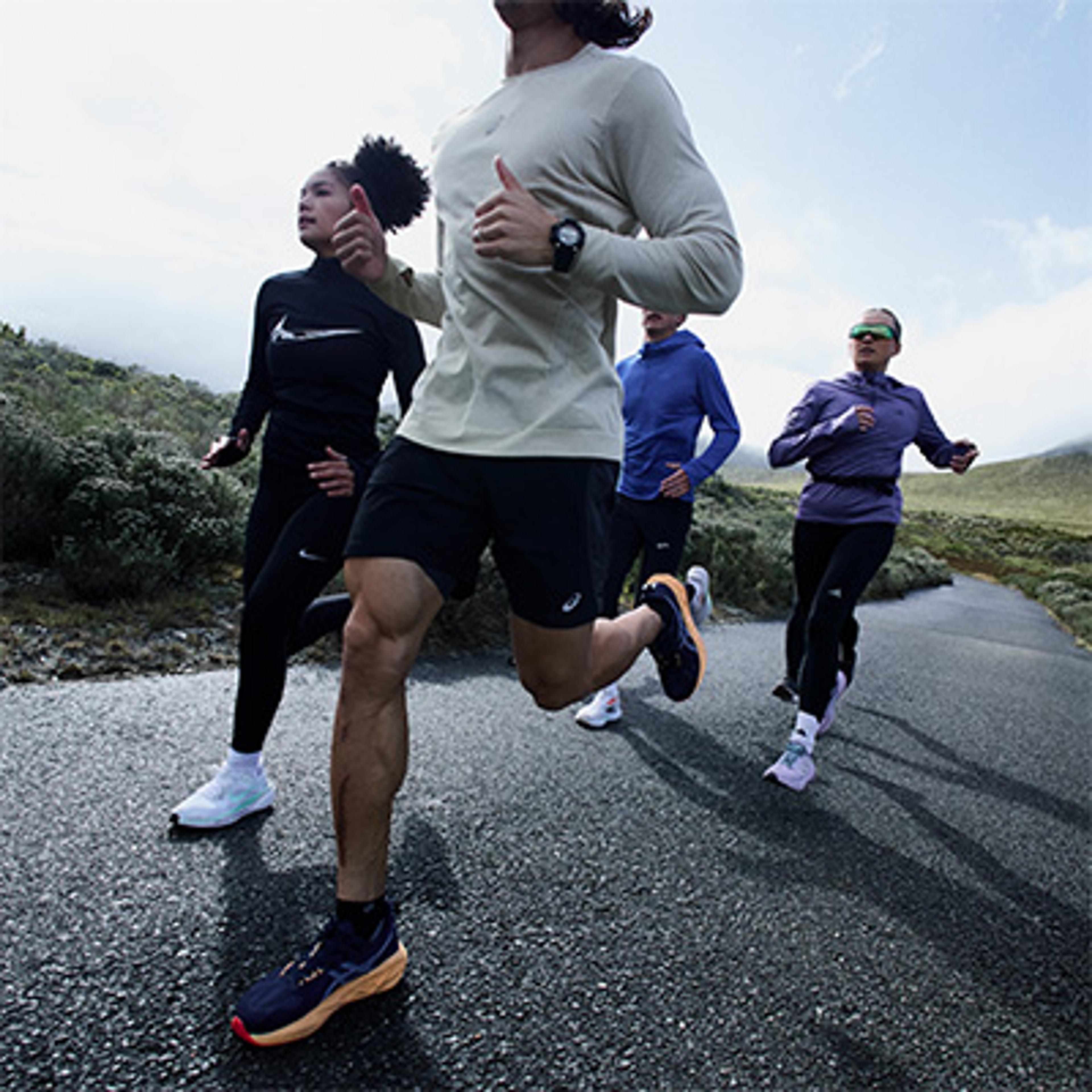 Four runners in athletic gear running on a paved road surrounded by hills.
