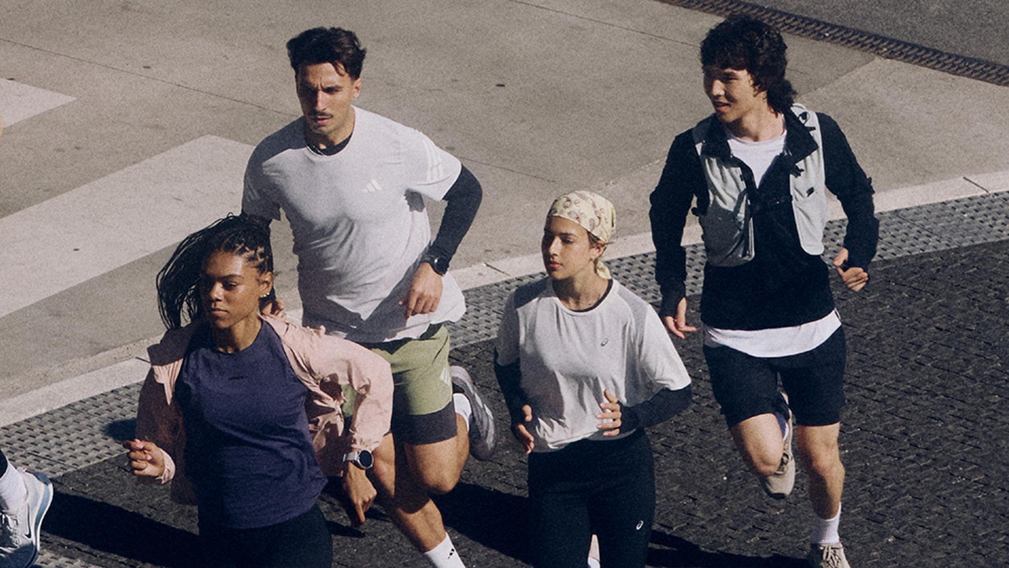 Four people in athletic gear running together on a paved street.