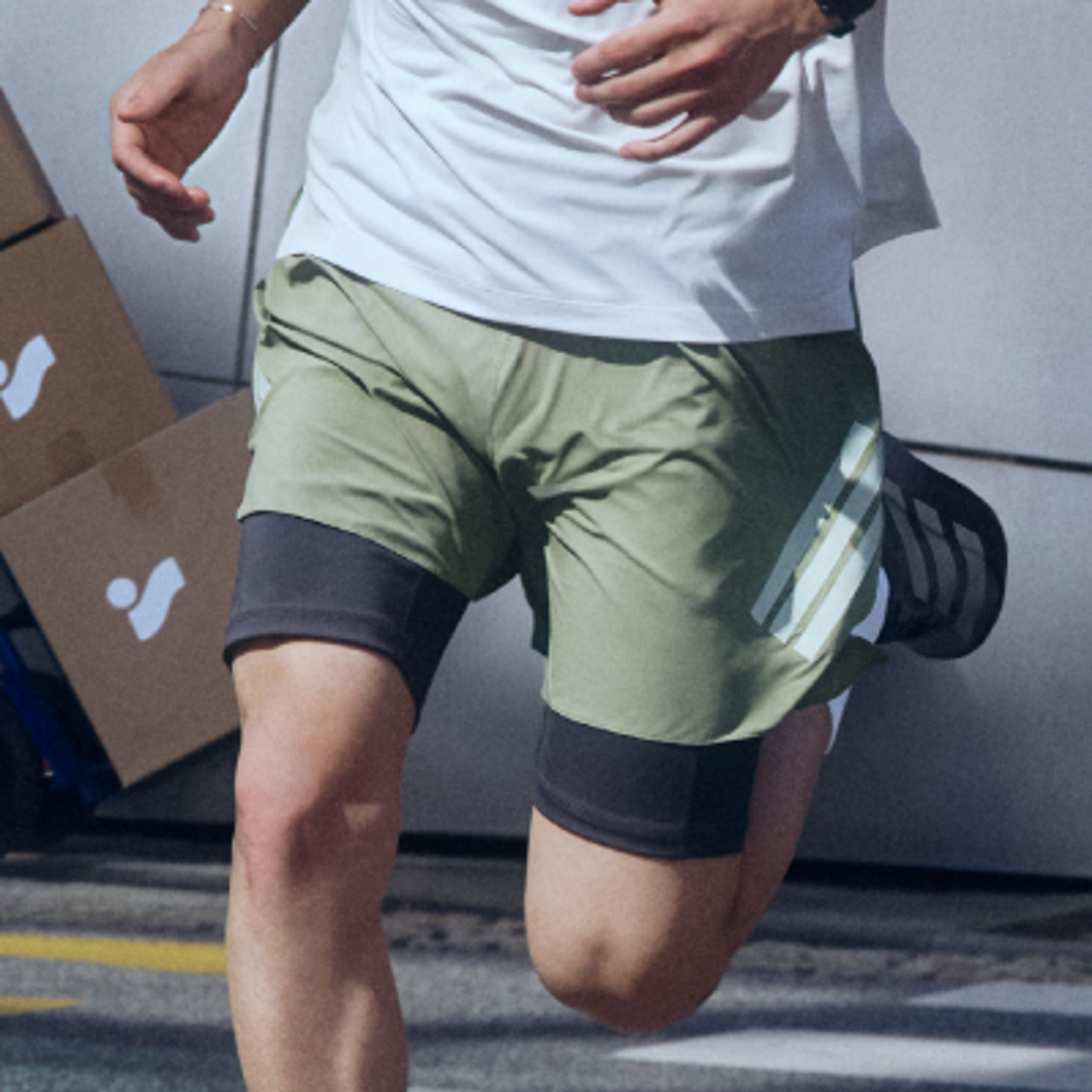 A person running, wearing a white t-shirt, olive green shorts, and black compression shorts.