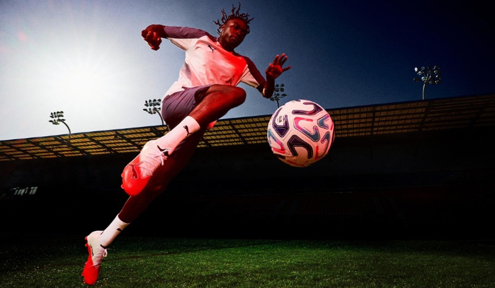 A soccer player leaps in the air next to a soccer ball on a stadium field.