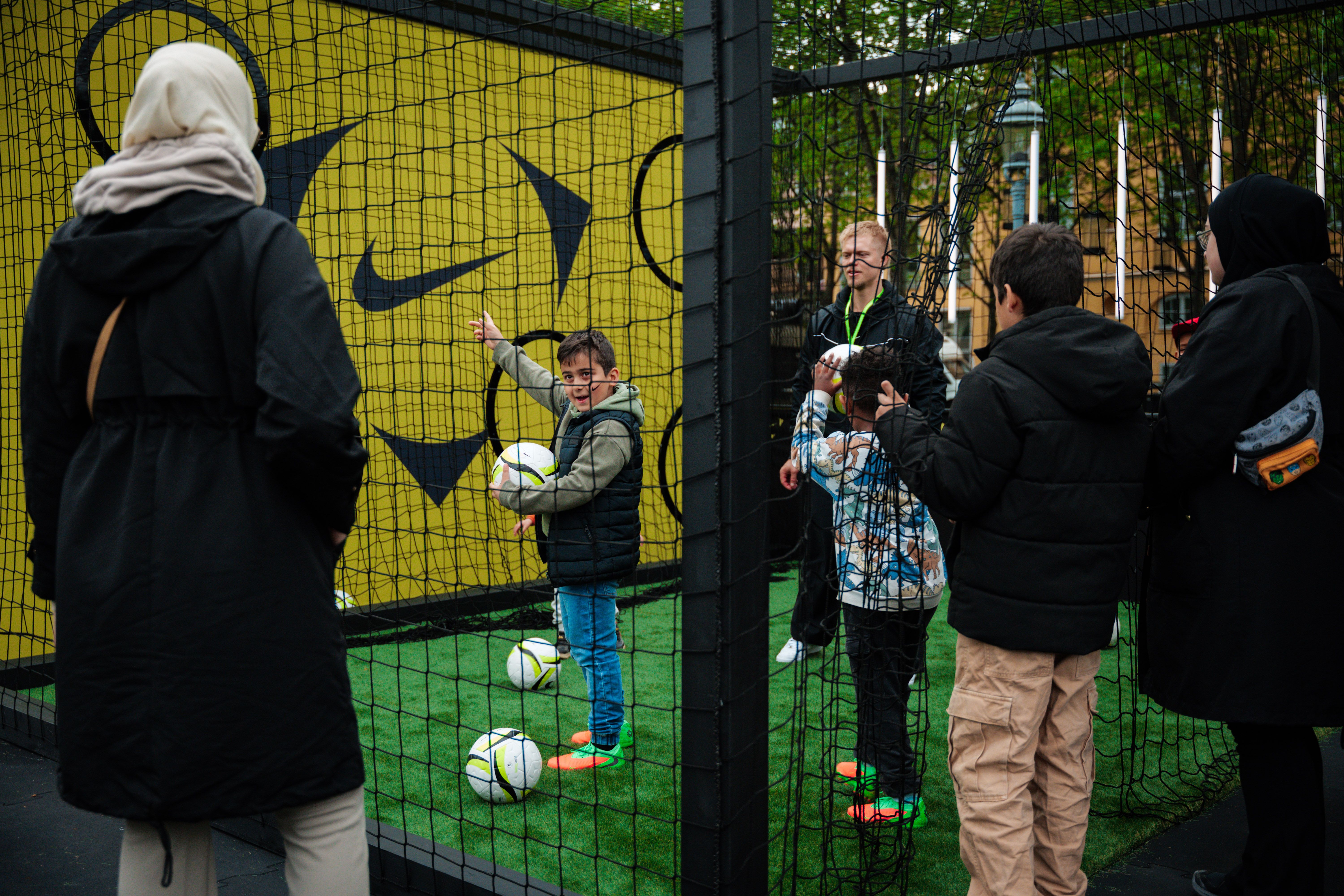Children and adults playing soccer in a netted, Nike-branded turf area.