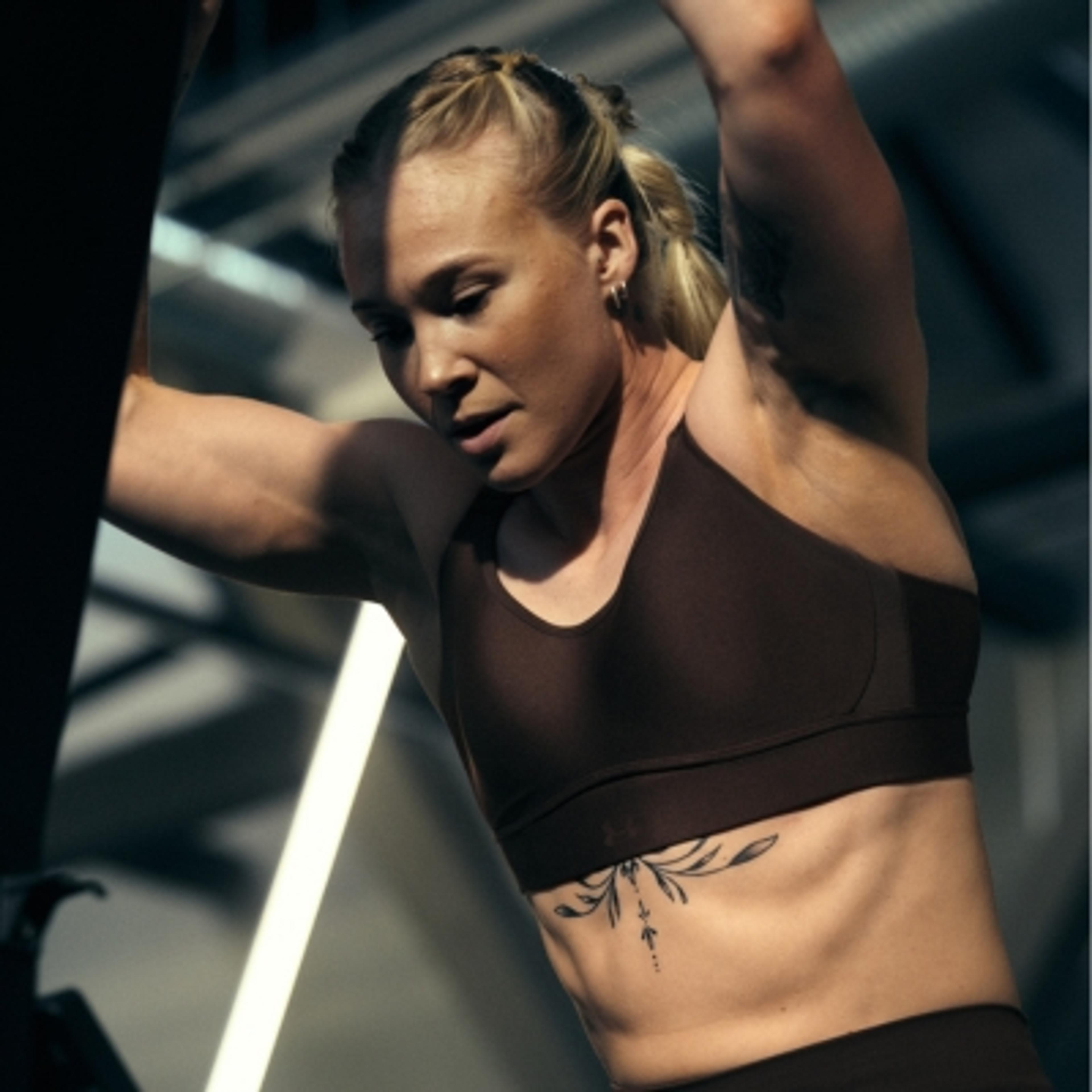 Muscular woman in a sports bra leaning, with a tattoo on her side.