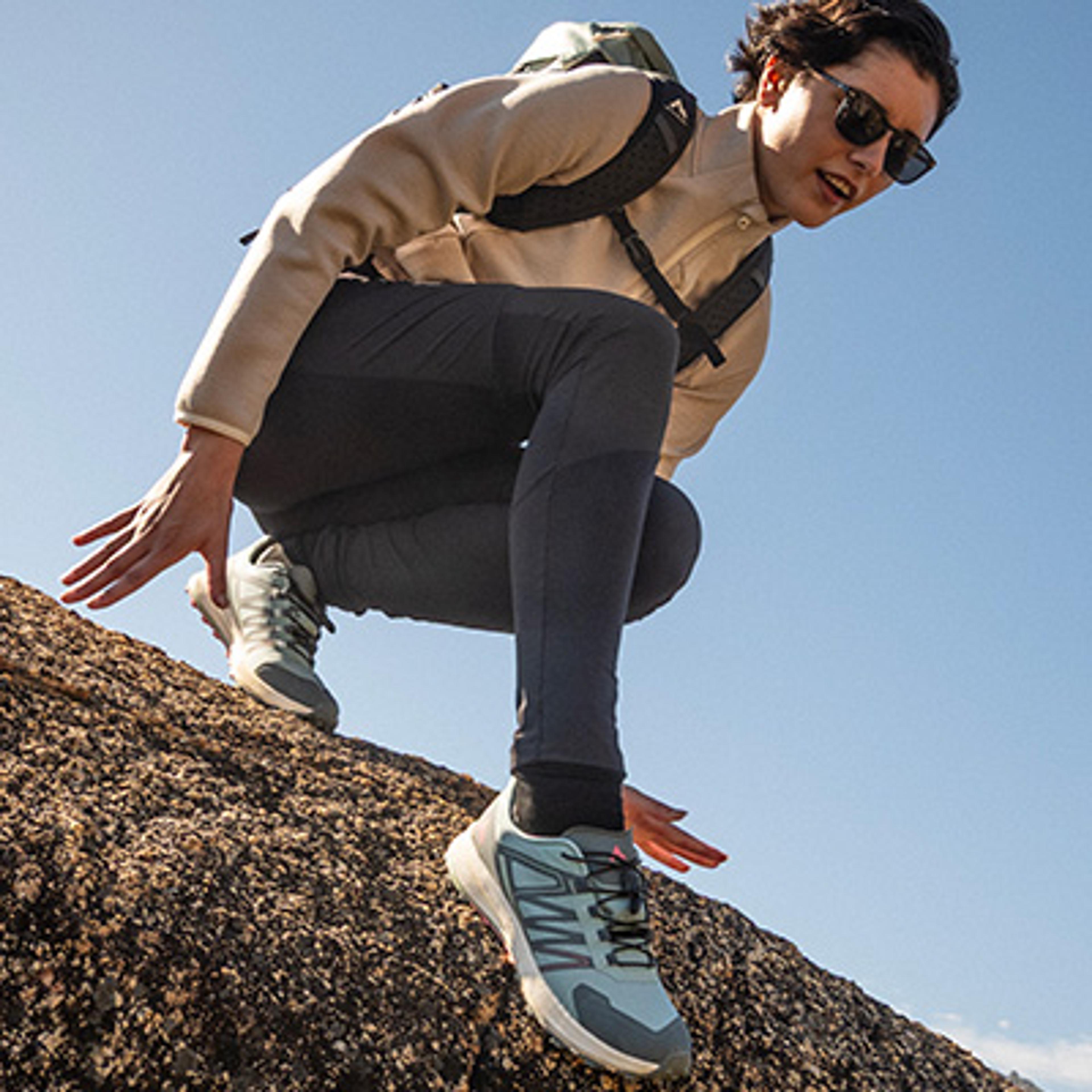 A hiker in sunglasses and a backpack steps down a rock.
