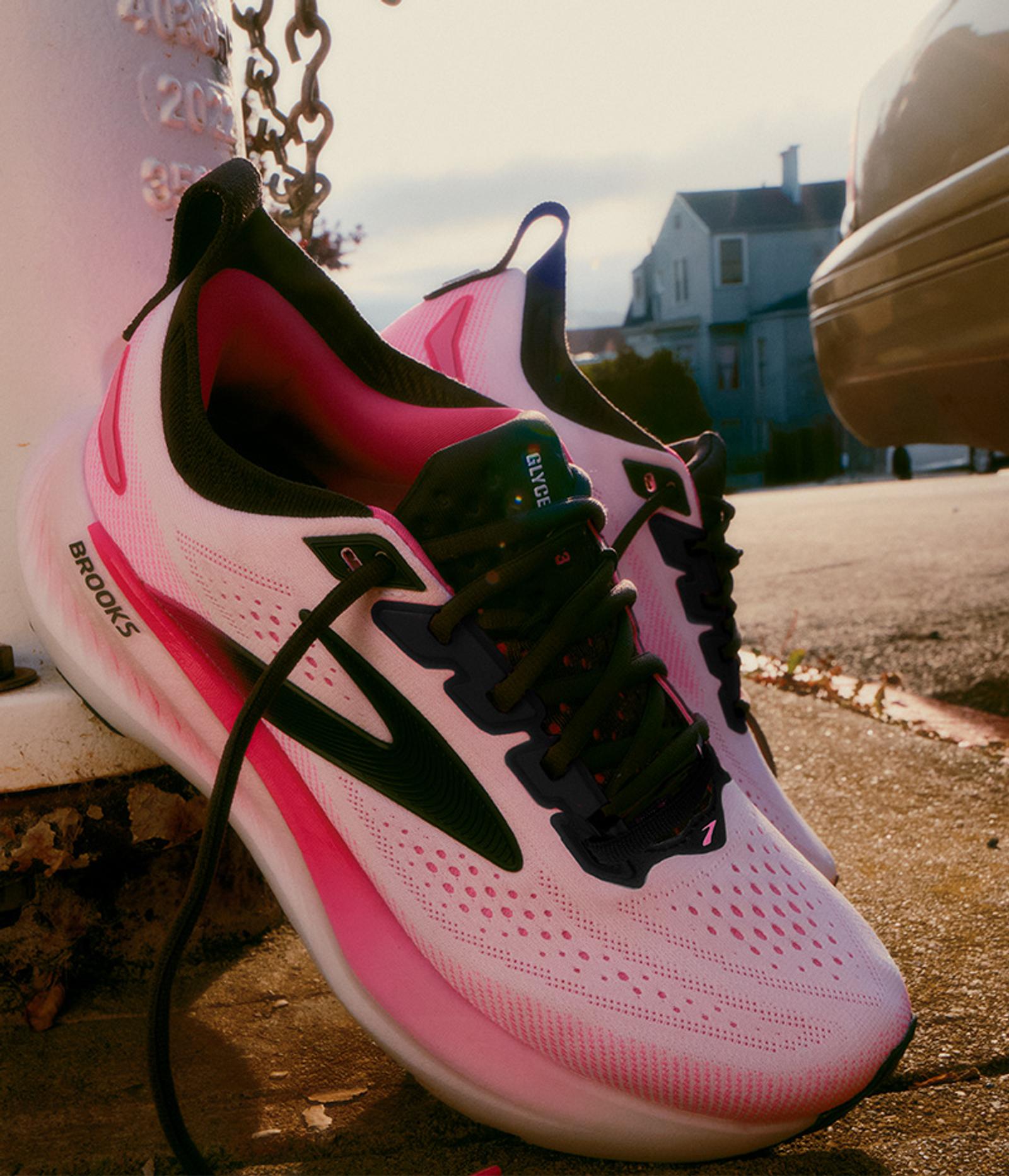 Pink Brooks Glyce running shoes leaning against a post outdoors.