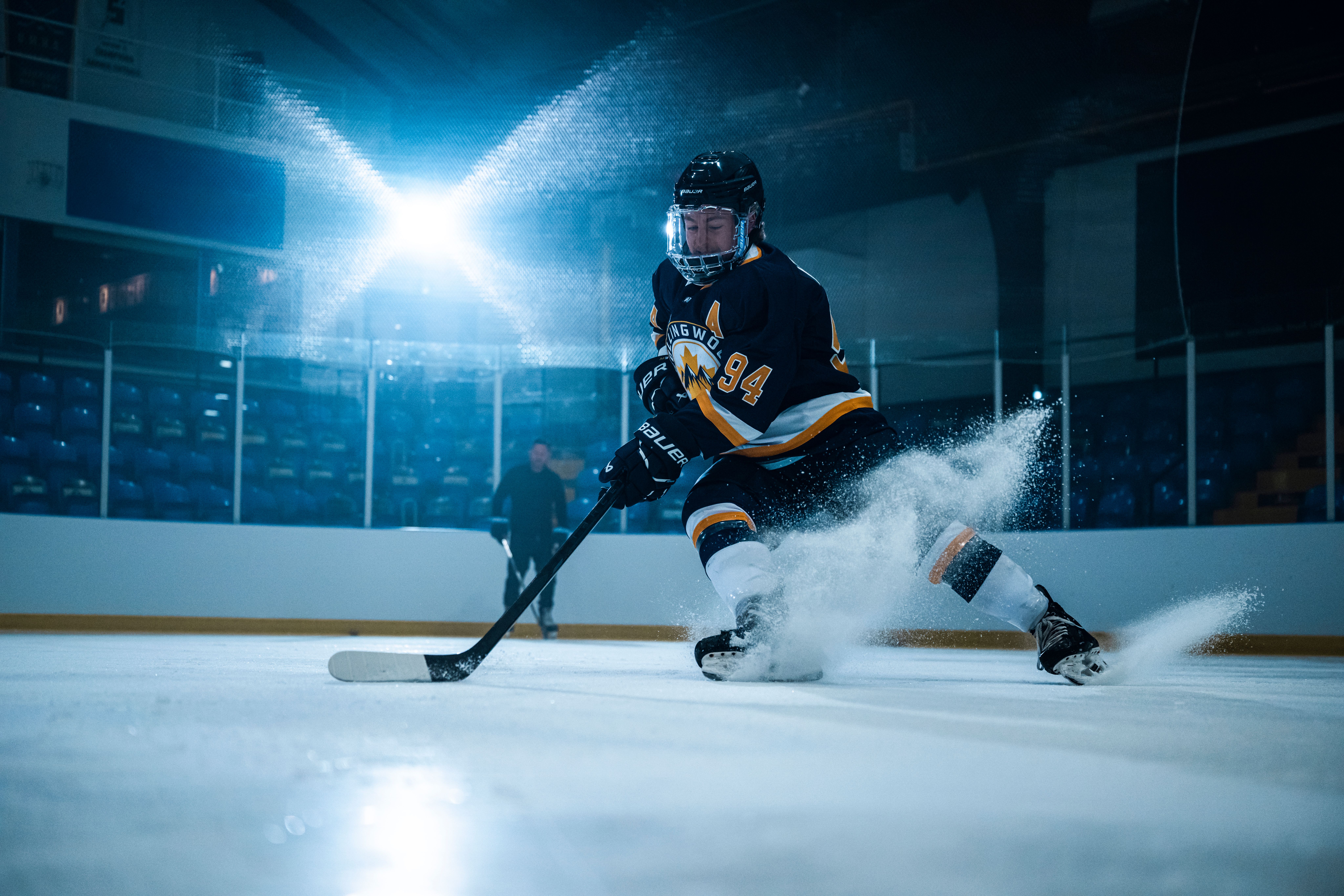 A hockey player in a black and yellow jersey kicks up a large spray of ice while skating in an arena.