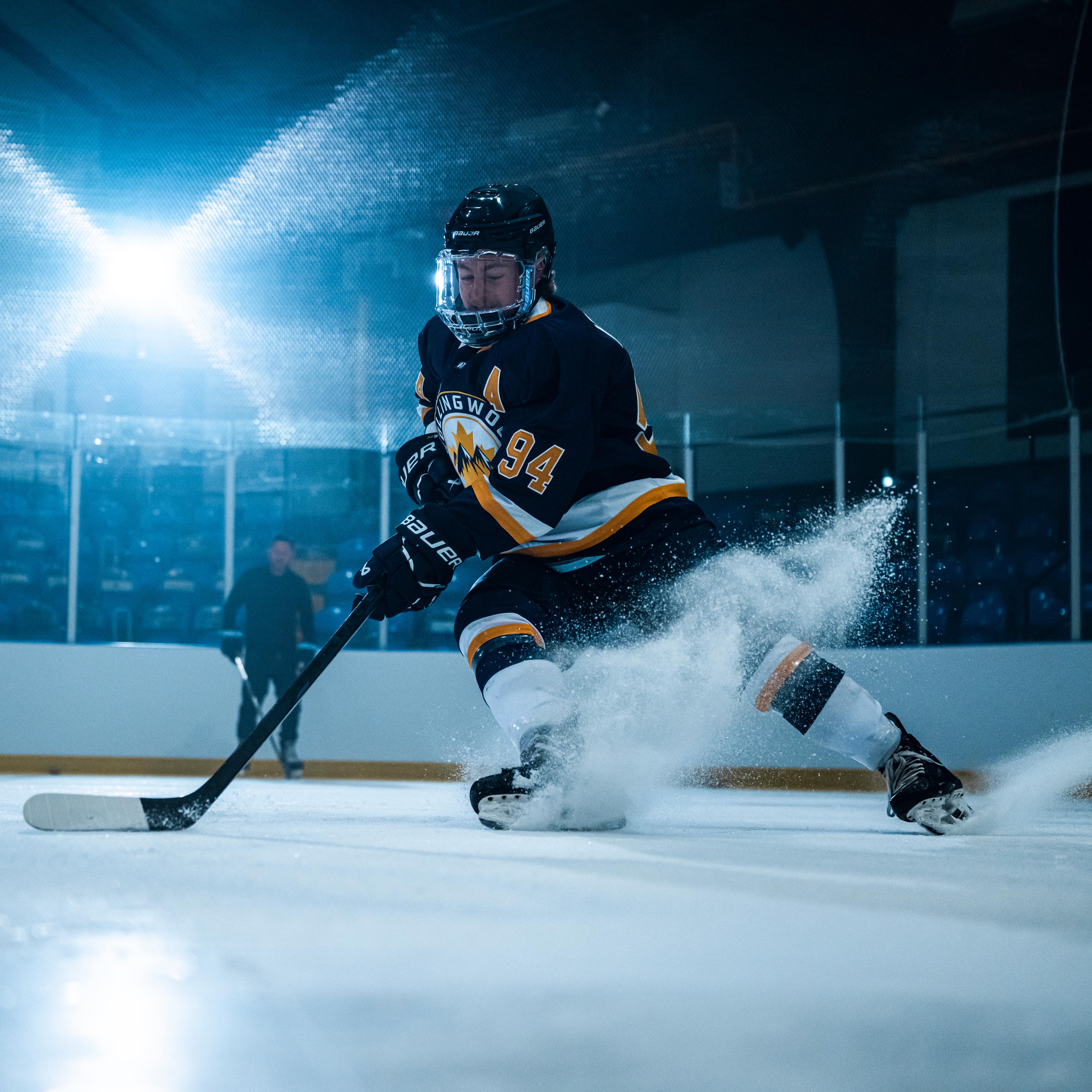 A hockey player in a black and yellow jersey kicks up a large spray of ice while skating in an arena.