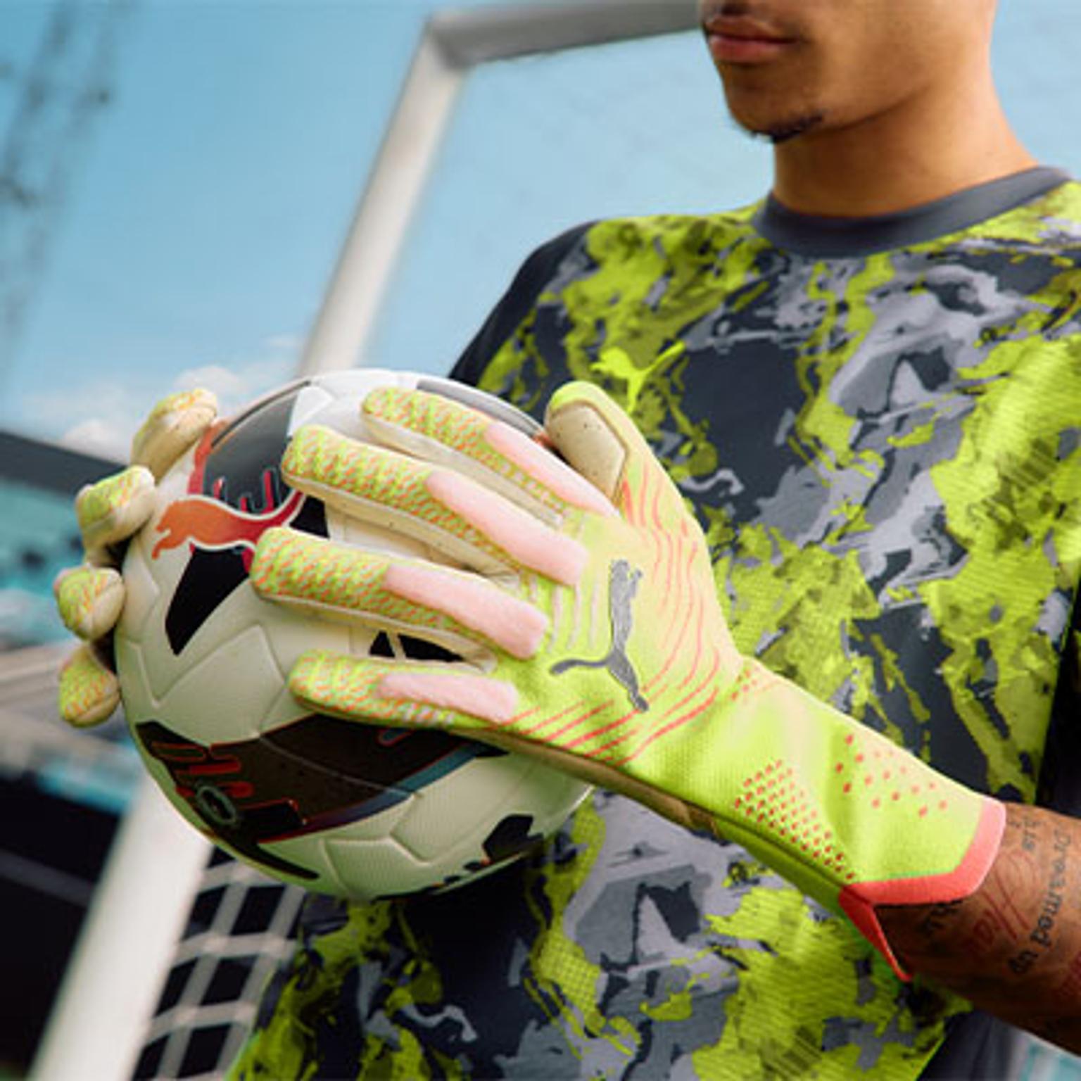 a man wearing a yellow and pink goalie glove is holding a soccer ball .