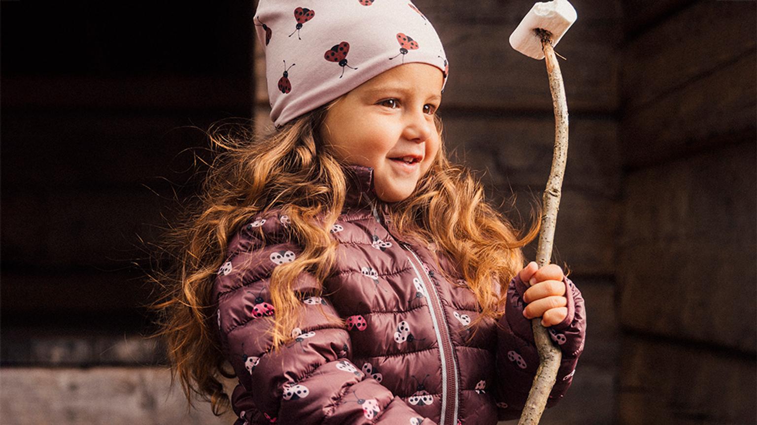 a little girl in a new jacket is holding a stick with a marshmallow on it .