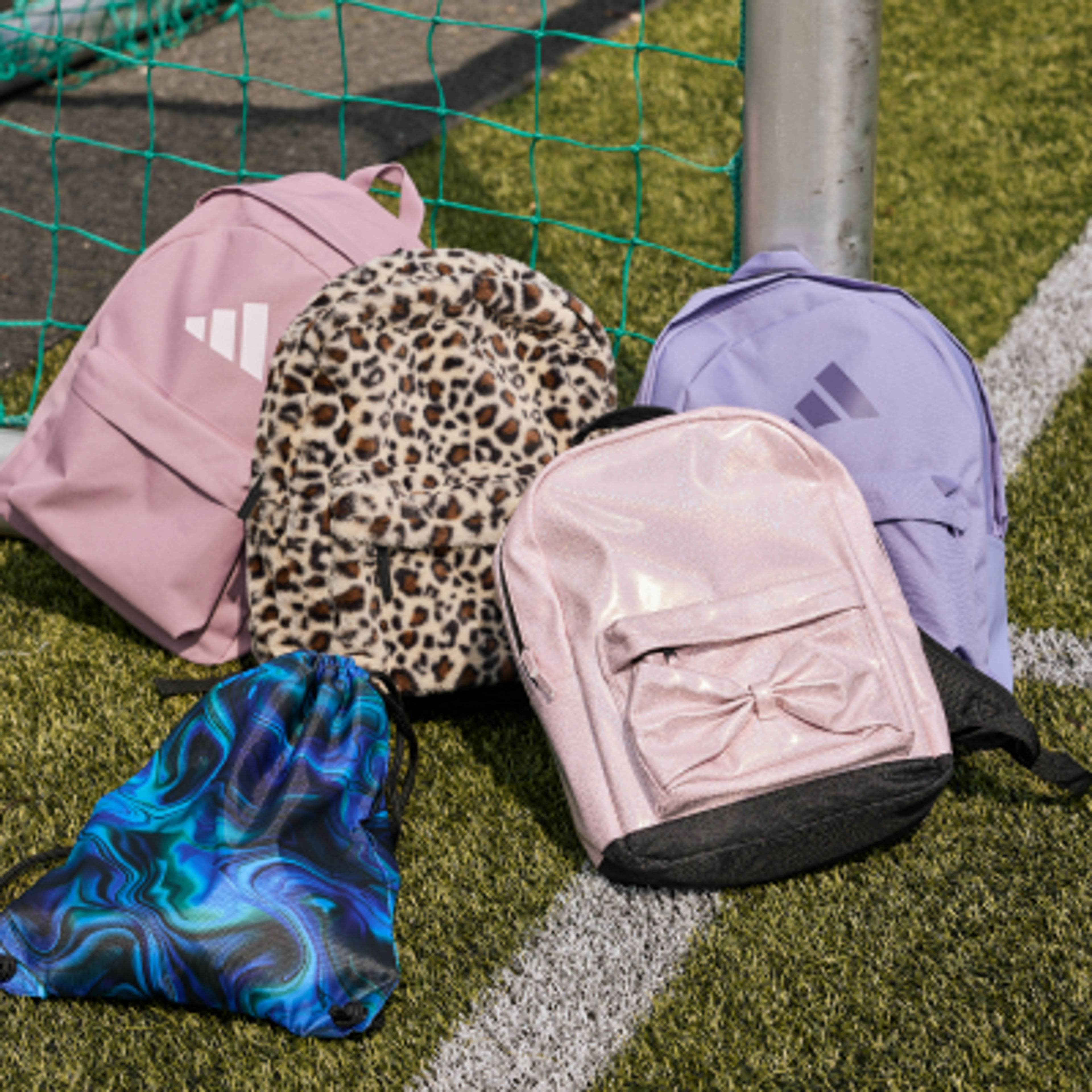Various backpacks and a patterned drawstring bag on a green sports field.